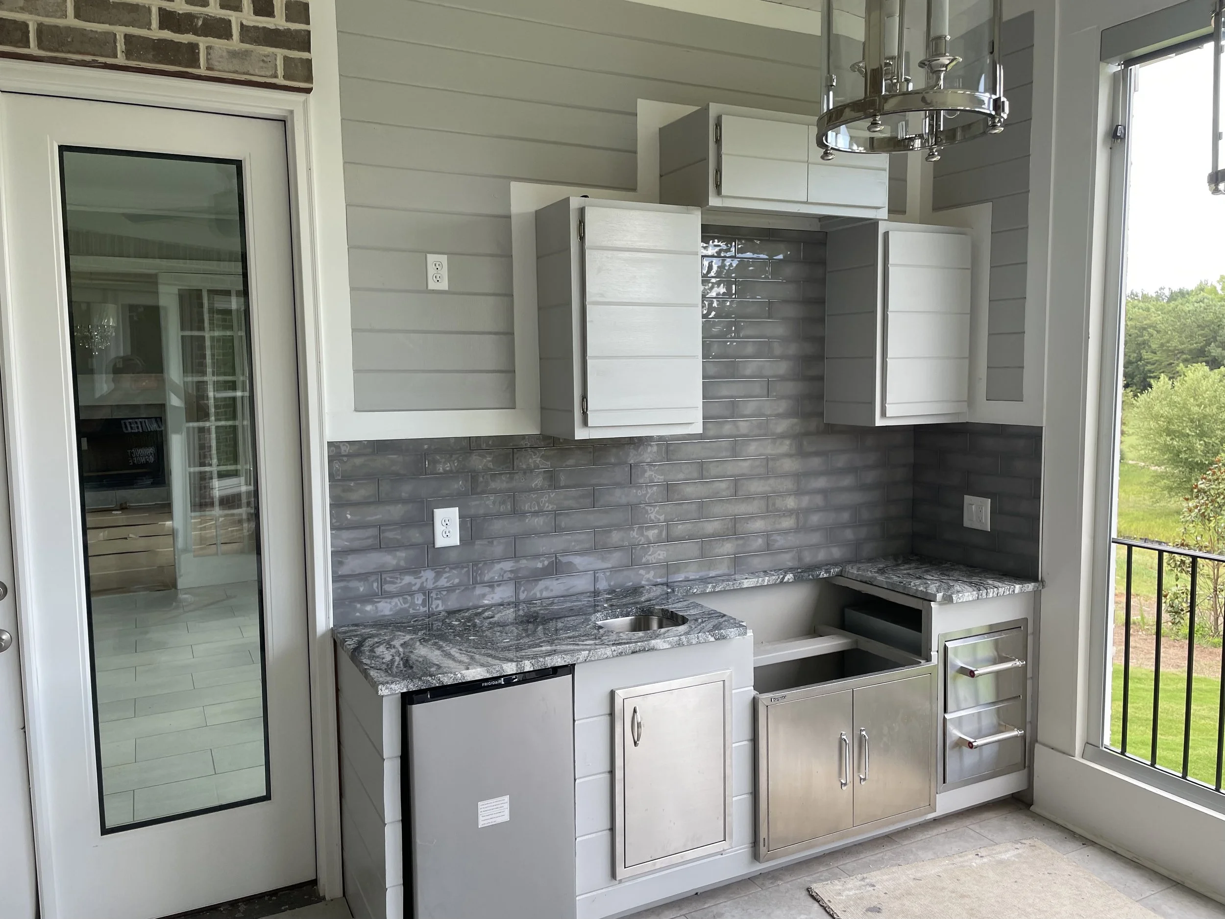 Custom outdoor kitchen backsplash featuring glossy gray subway tiles that beautifully complement the white cabinetry and stone countertops, creating a sleek and modern finish.