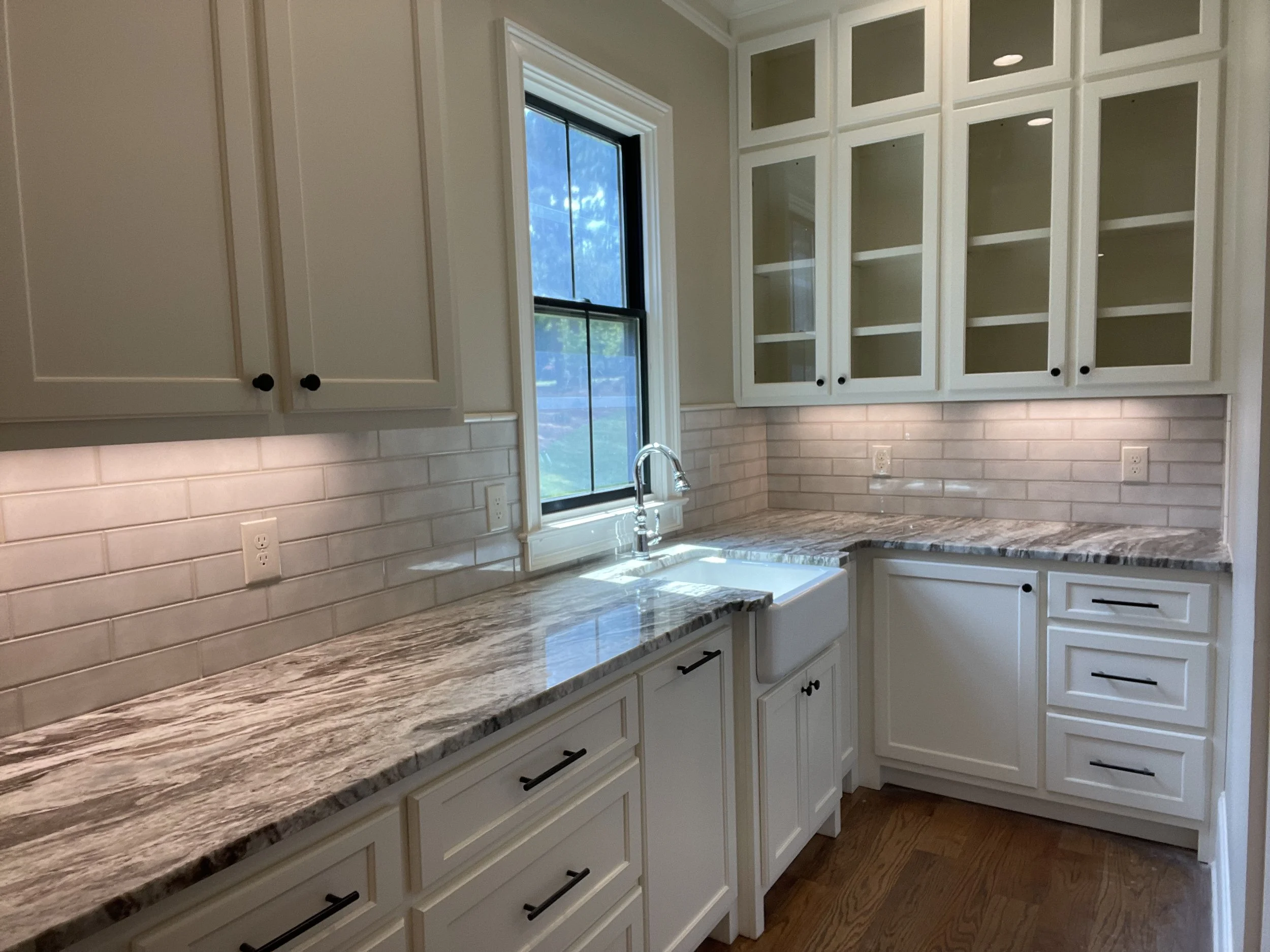Kitchen with white cabinets, granite countertops, a window above the sink, and a white subway tile backsplash.