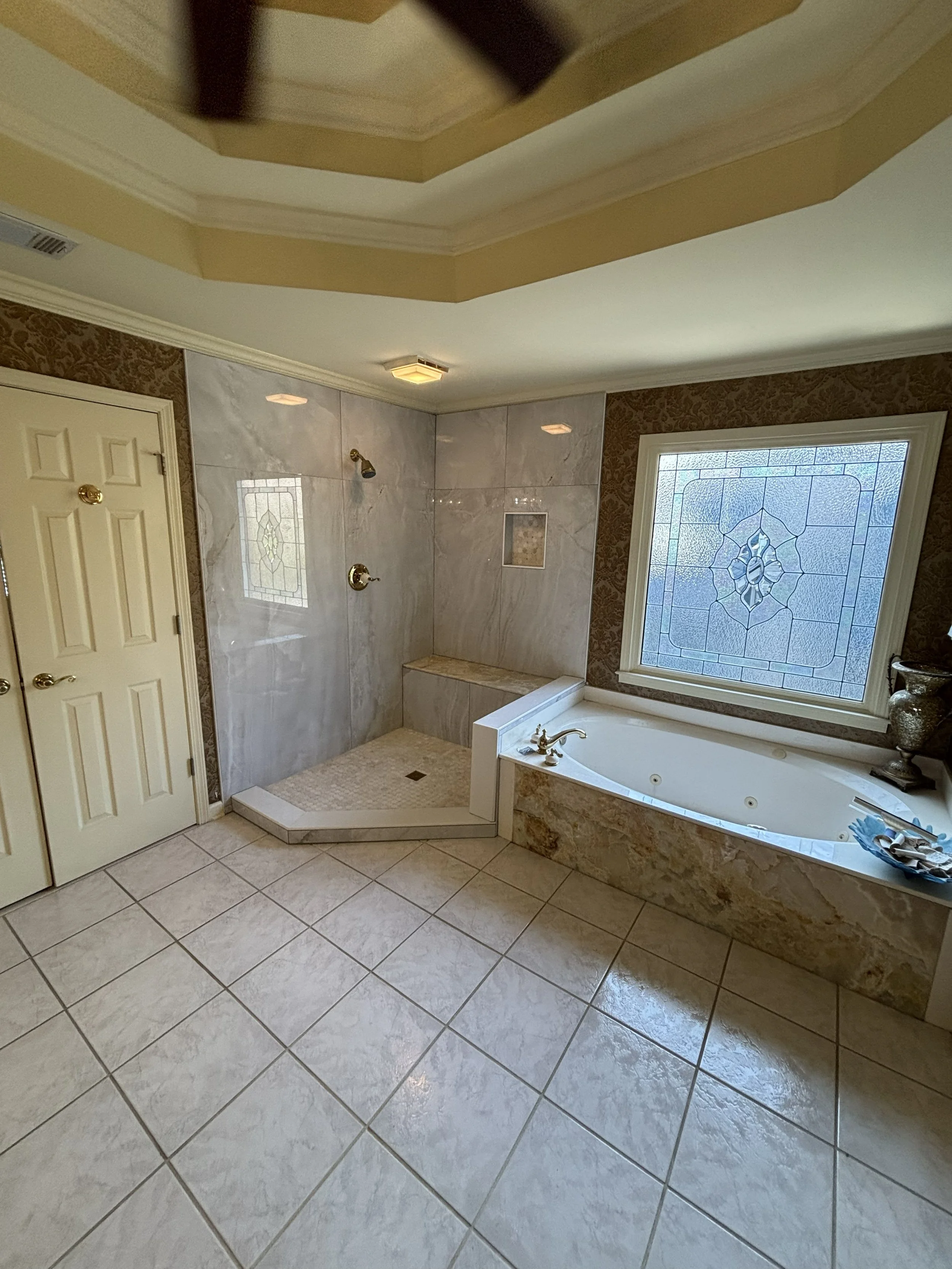 Bathroom with a large window, bathtub, tiled shower area, and beige tile flooring.