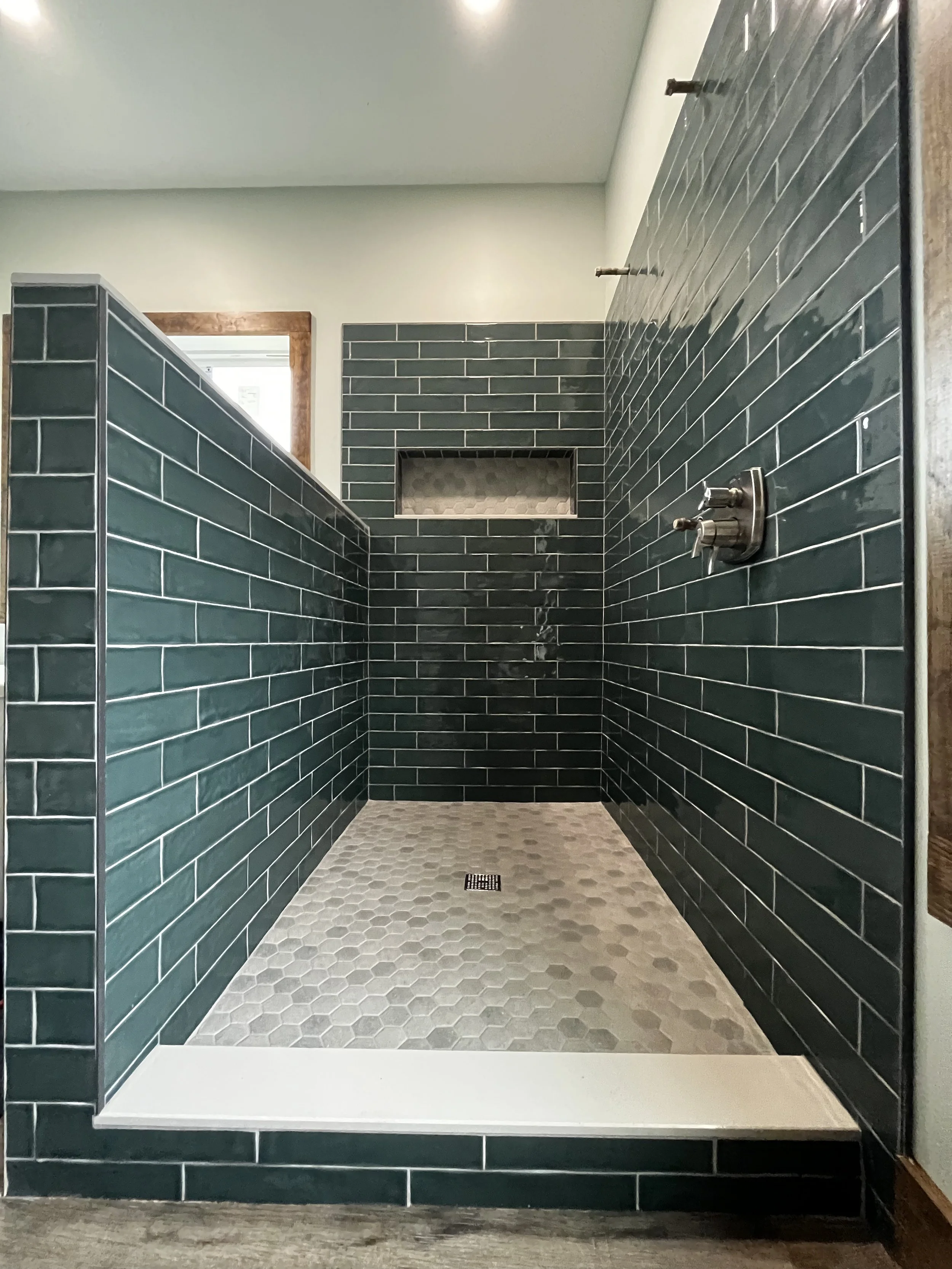 A modern walk-in shower with dark green subway tile walls, a hexagonal tiled floor, a built-in niche, and a rain showerhead.