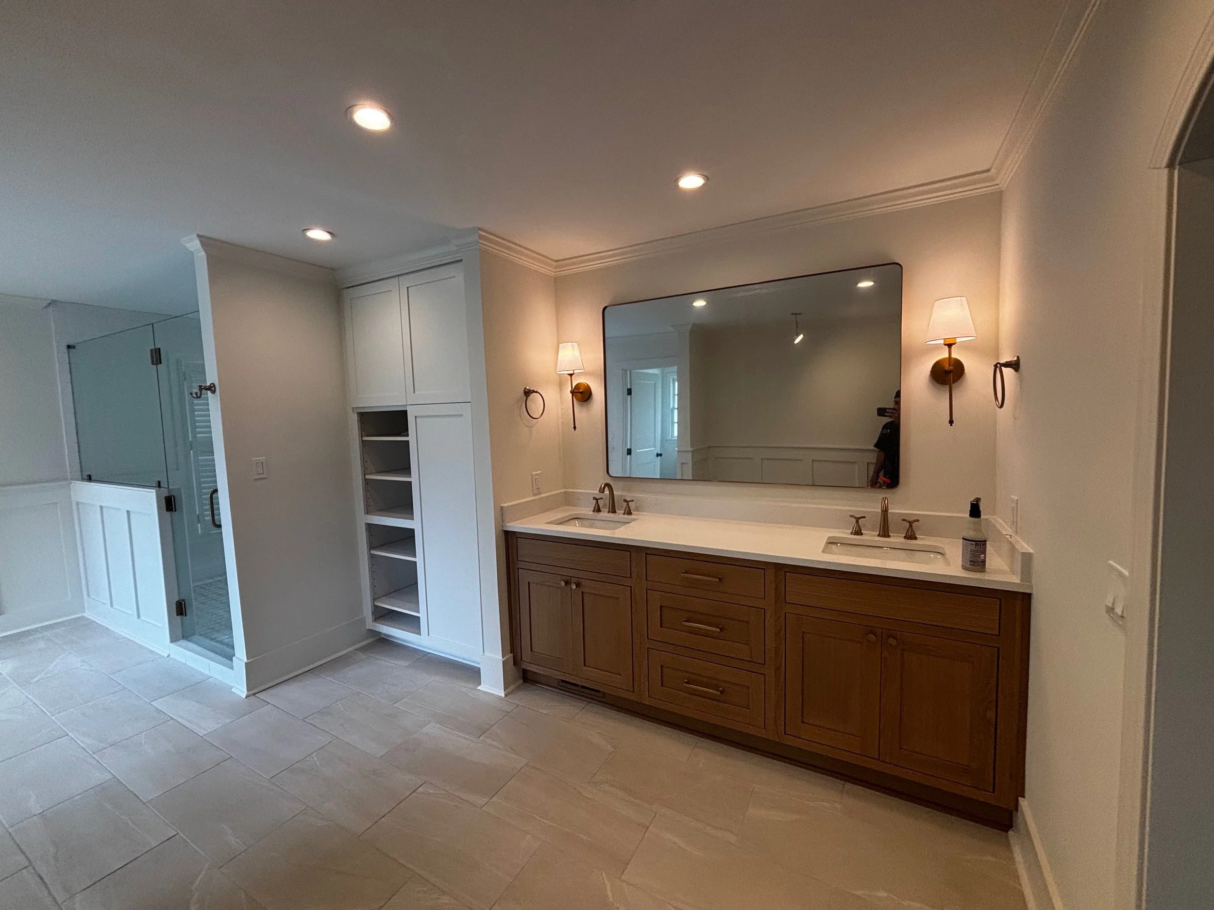 Bathroom with double sink vanity, large mirror, wall-mounted lamps, and a glass shower enclosure.