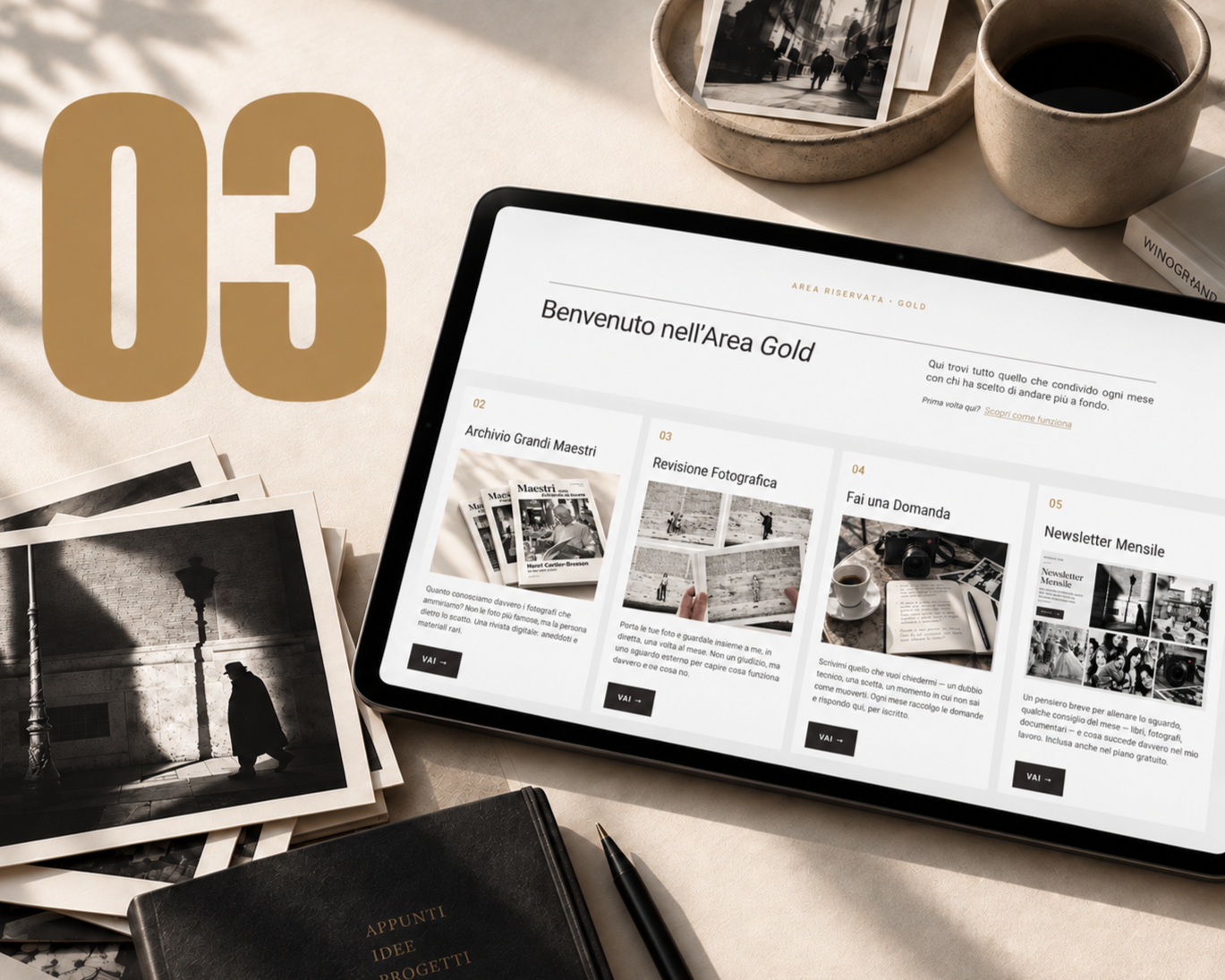 Tablet con la home page dell'Area Gold, circondato da stampe fotografiche in bianco e nero e taccuini, su una scrivania con una tazza di caffè.