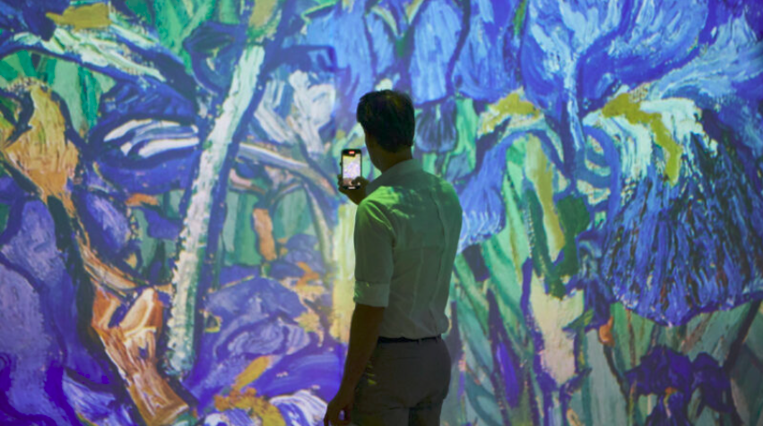 A man taking a photo of vibrant, abstract artwork with a smartphone.