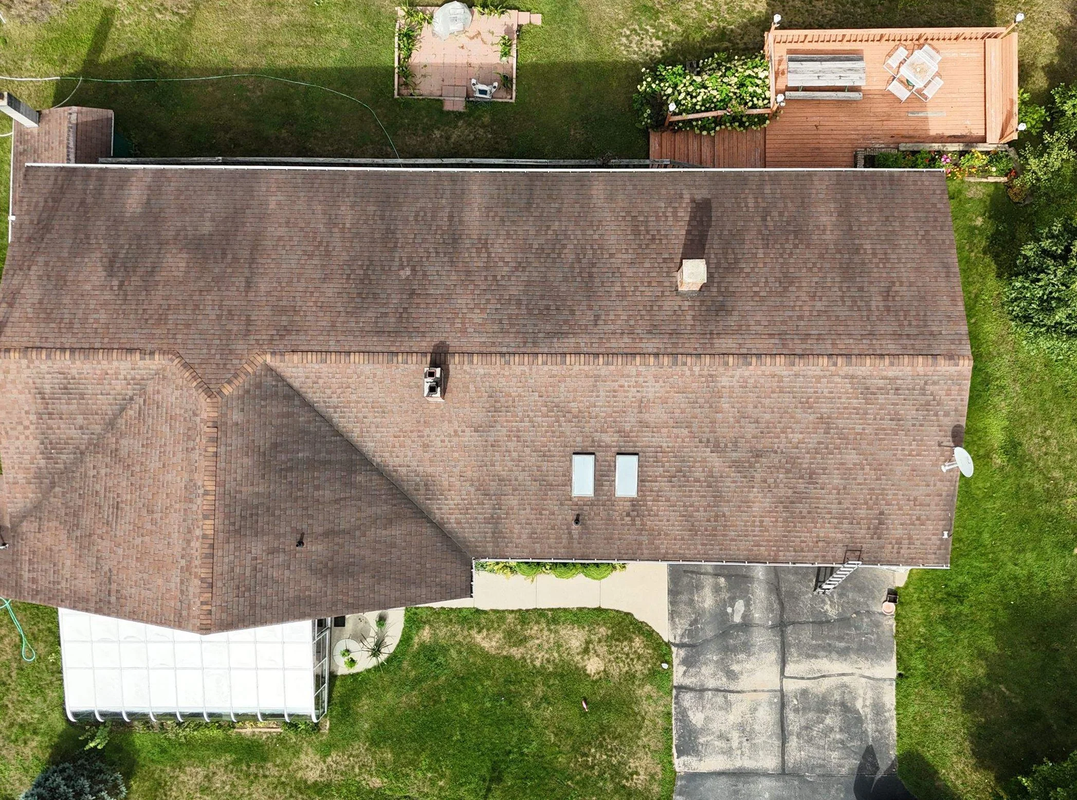 Aerial view of a house with a brown shingled roof, small backyard, and a paved driveway.