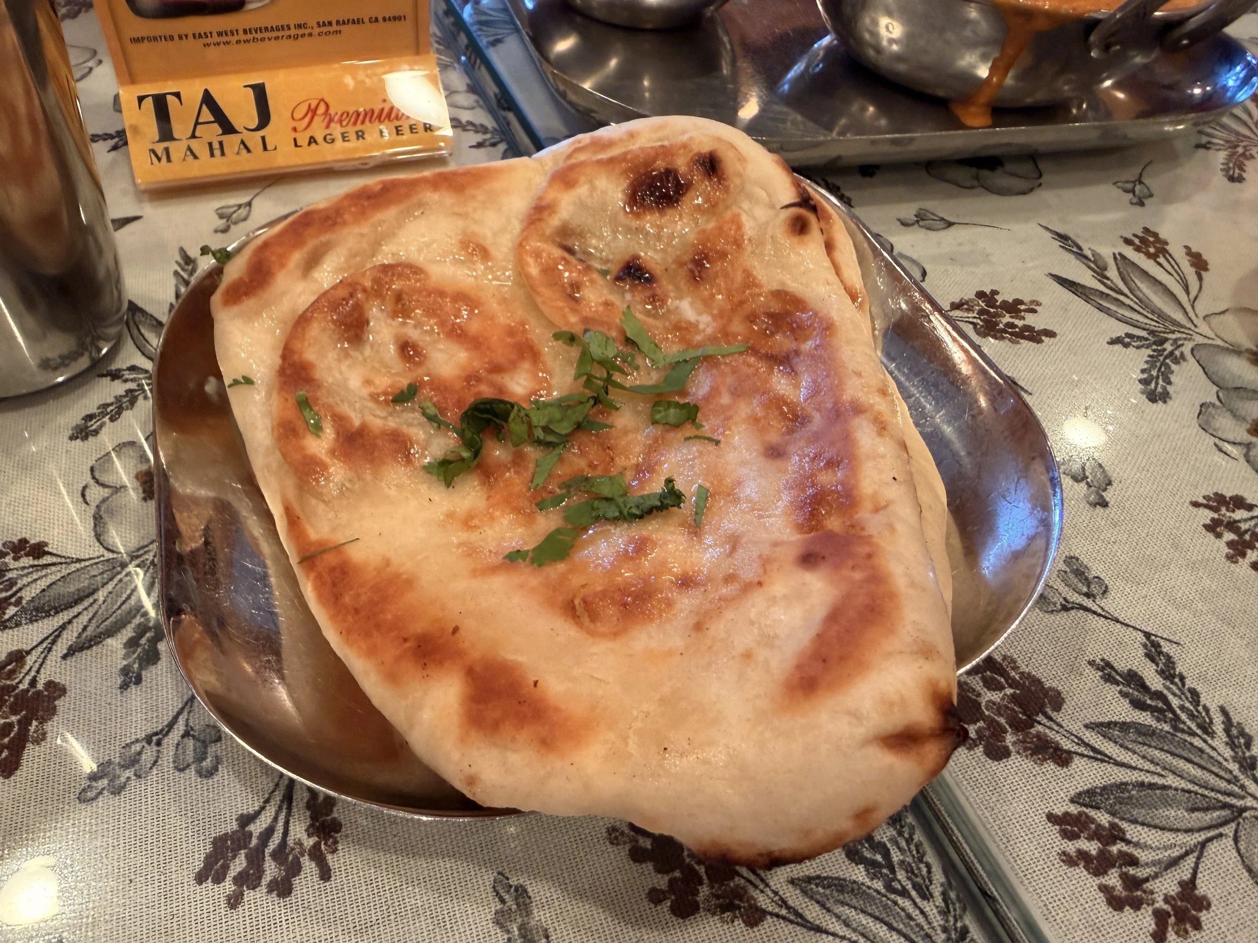 A close-up shot of a freshly baked, pillowy butter naan garnished with cilantro on a metal plate.