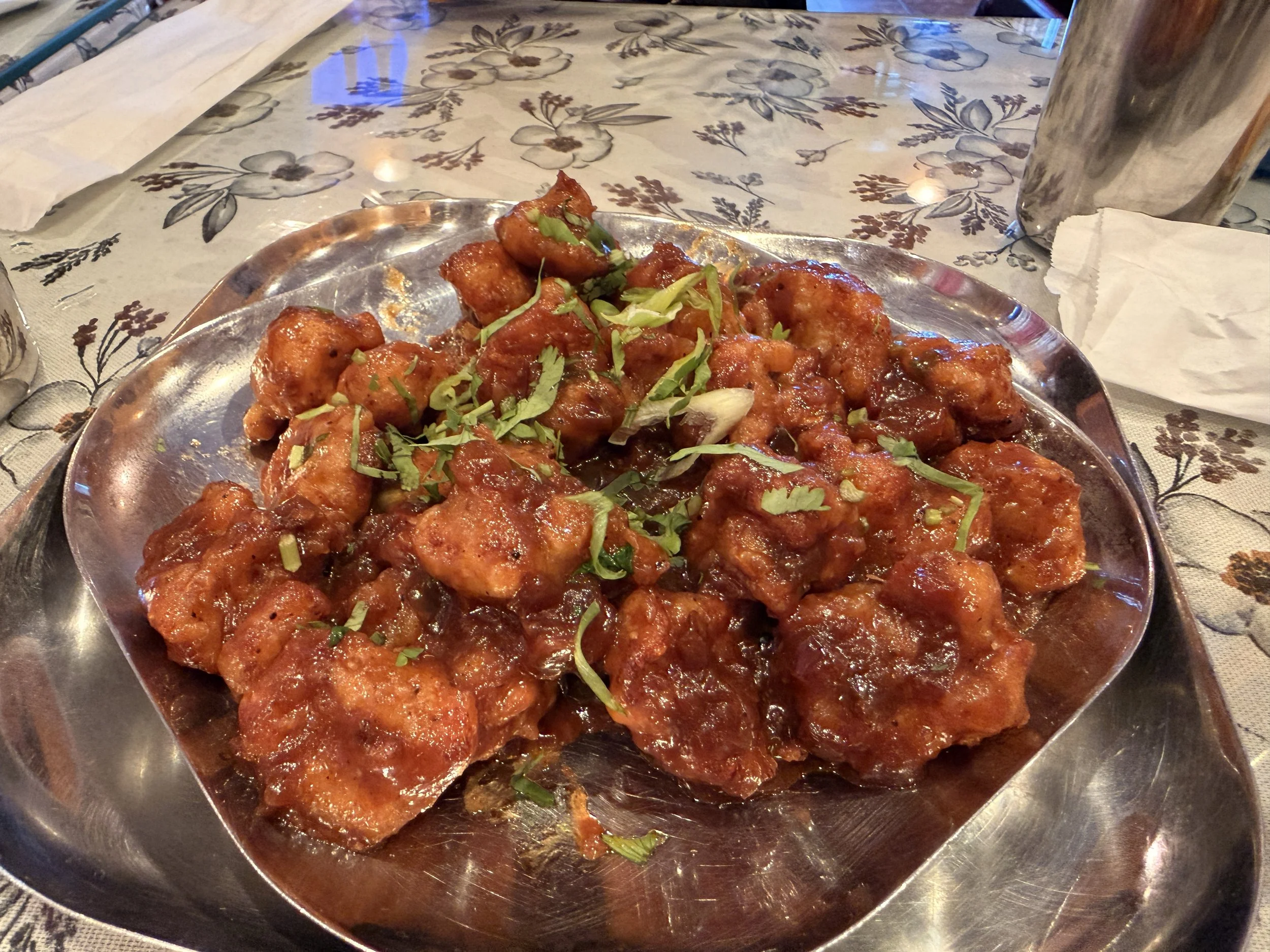 A silver platter piled high with crispy, deep-red Indo-Chinese Gobi Manchurian garnished with scallions and cilantro.