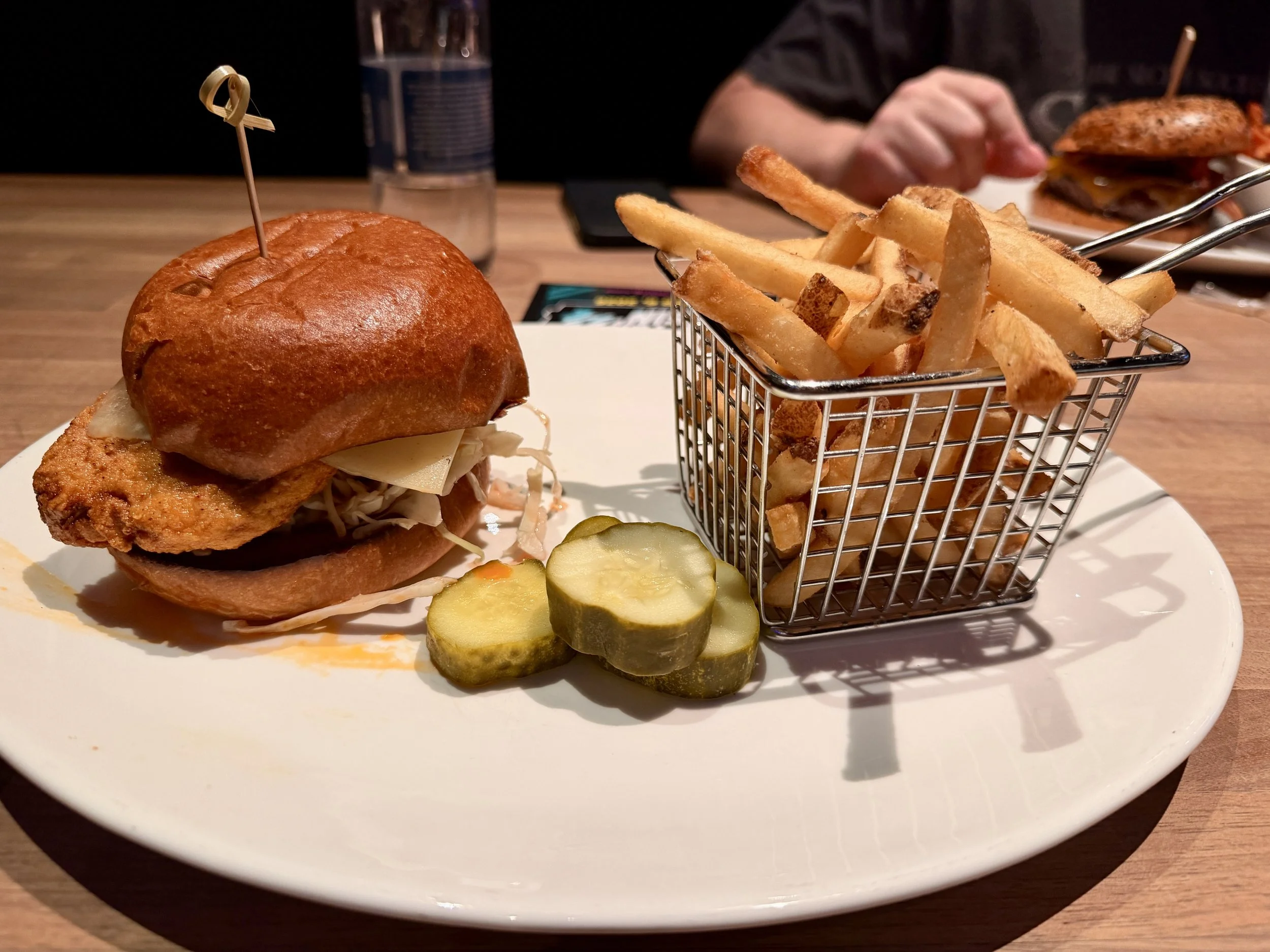 Gardein Nashville Hot Chicken Sandwich at Yard House served on a white plate with French fries in a wire basket and pickle slices