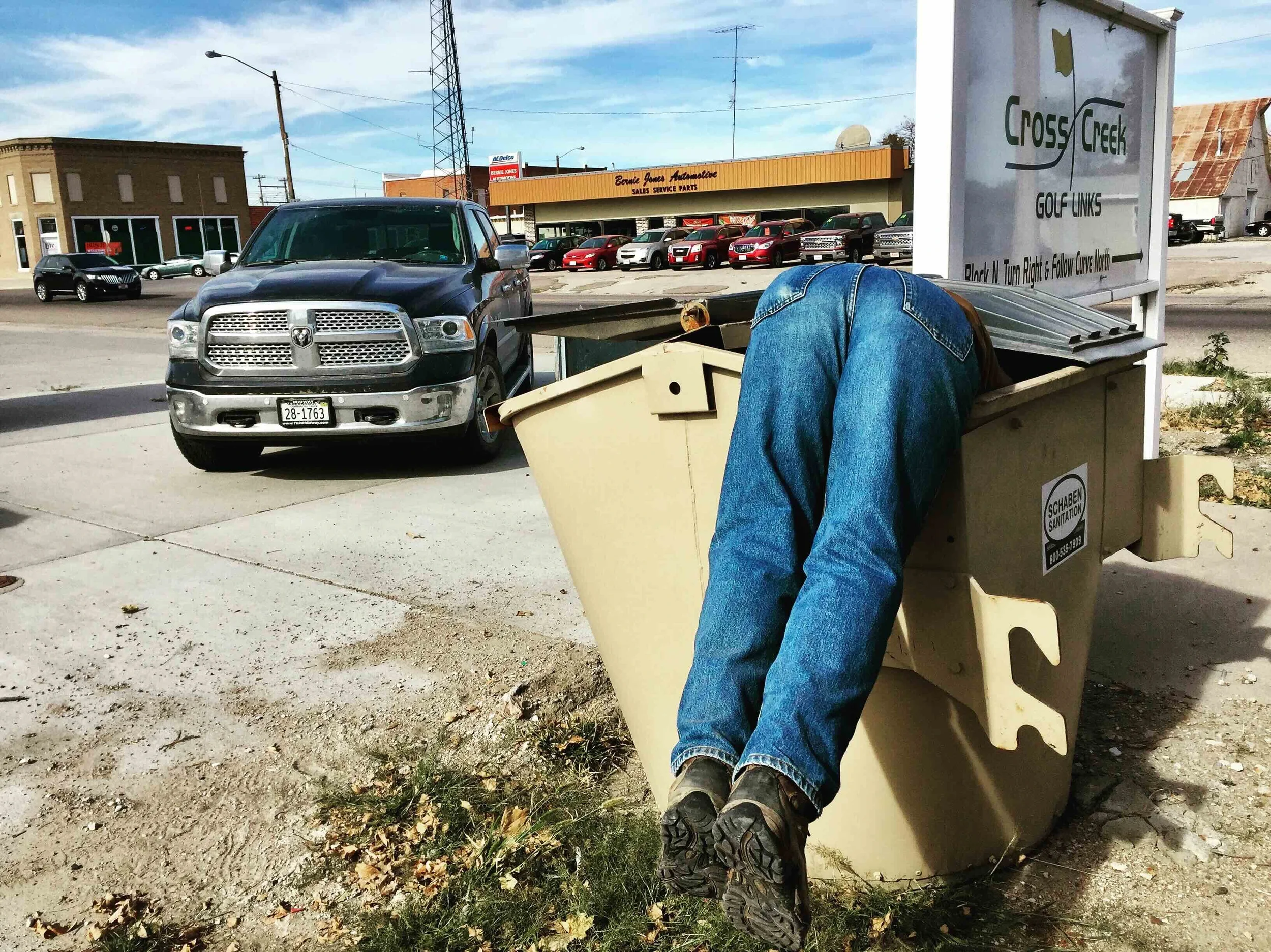 Person with jeans and work boots bent into a trash receptacle, with only their legs and torso visible.