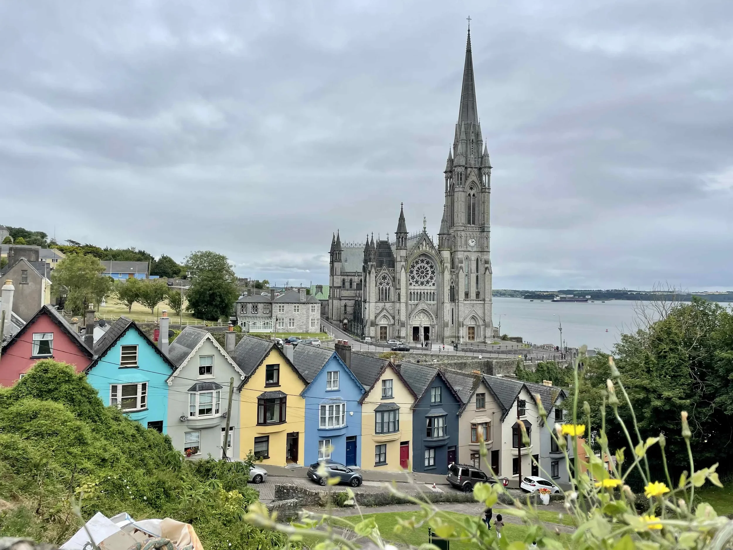 Colorful row of houses with a gray Gothic-style church and water in the background under a cloudy sky.