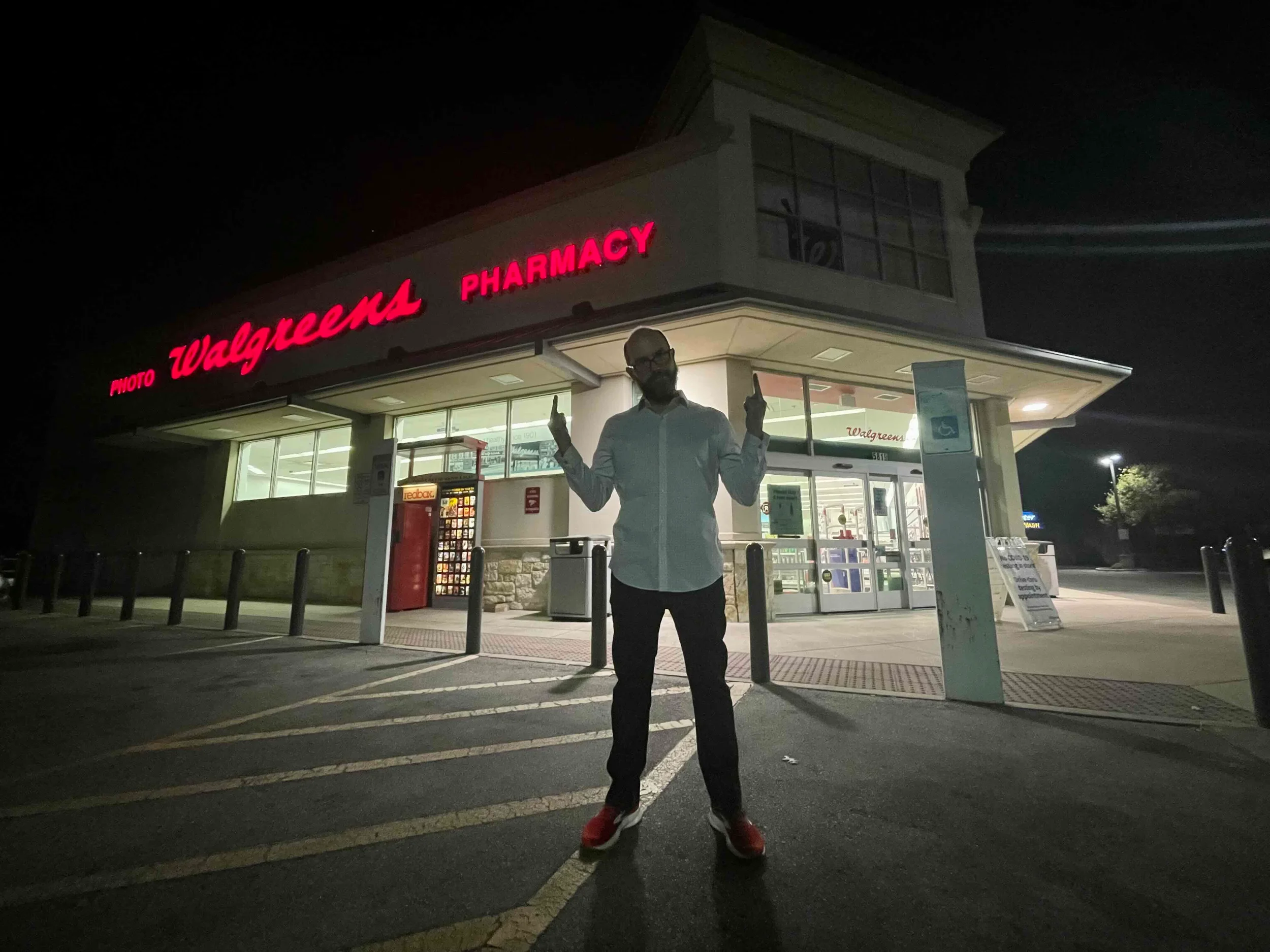 A person standing in front of a Walgreens pharmacy at night, illuminated from inside, with the Walgreens sign in red above.