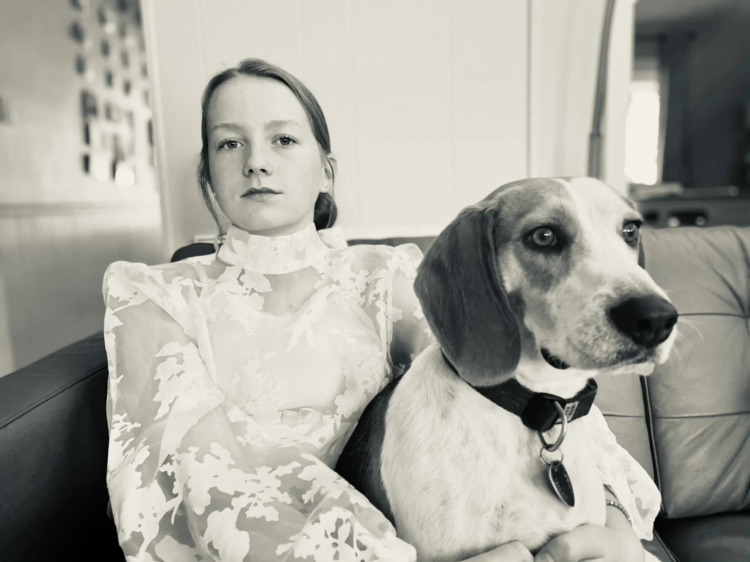 Black and white photo of a young girl with long hair and a serious expression sitting on a couch with a beagle dog.