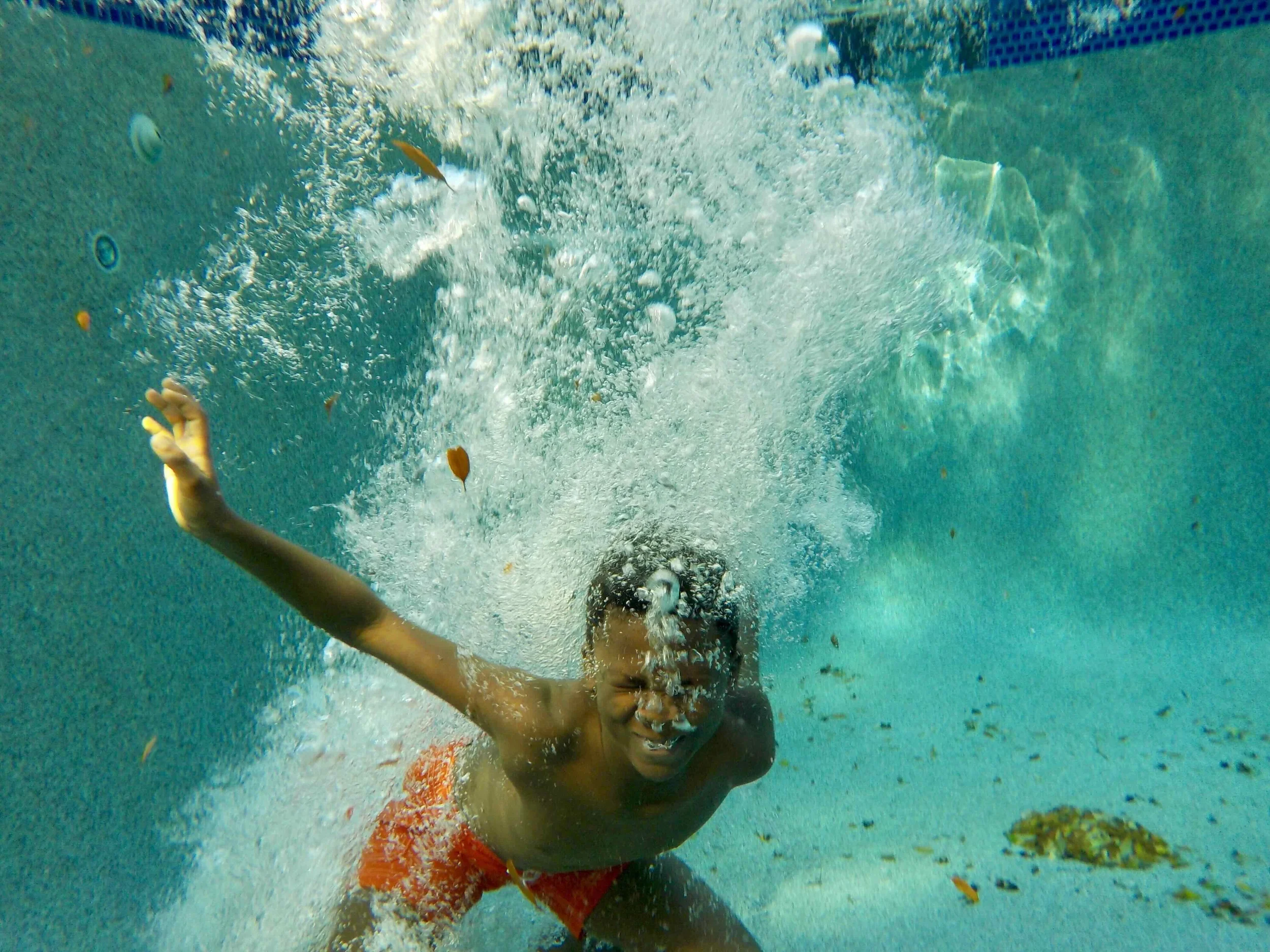 Child swimming underwater in a pool, smiling and making a playful gesture with their hand.