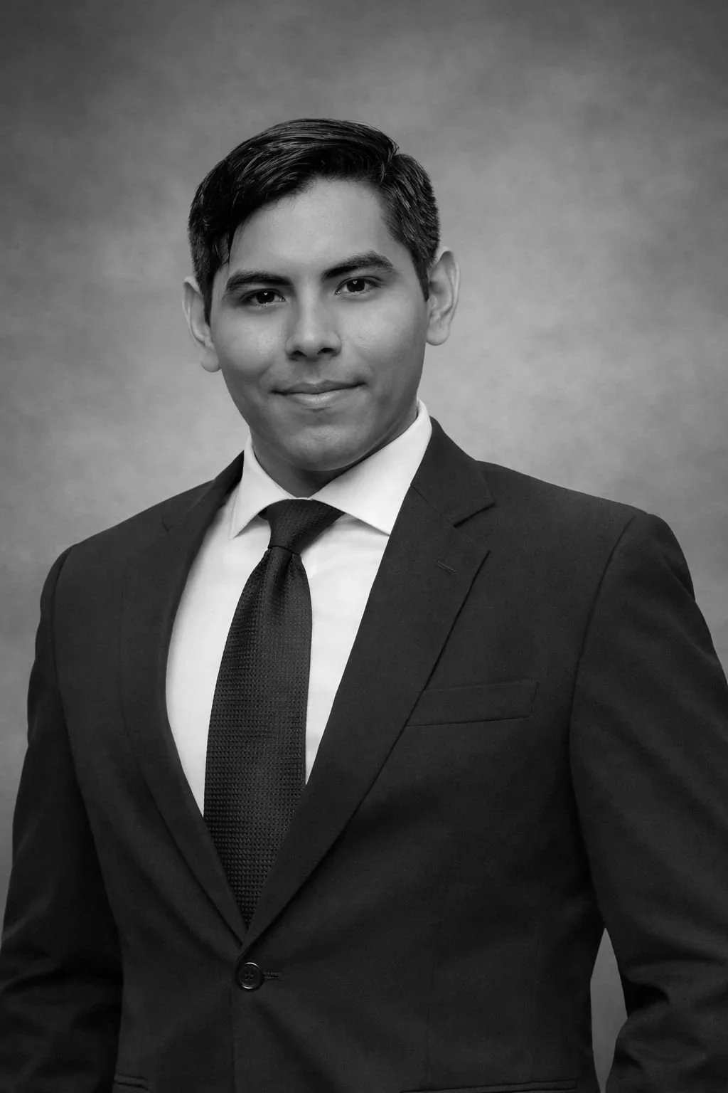 Retrato en blanco y negro de un hombre con cabello oscuro, peinado hacia un lado, vestido con traje formal, camisa blanca y corbata, sonriendo ligeramente, frente a un fondo neutro.