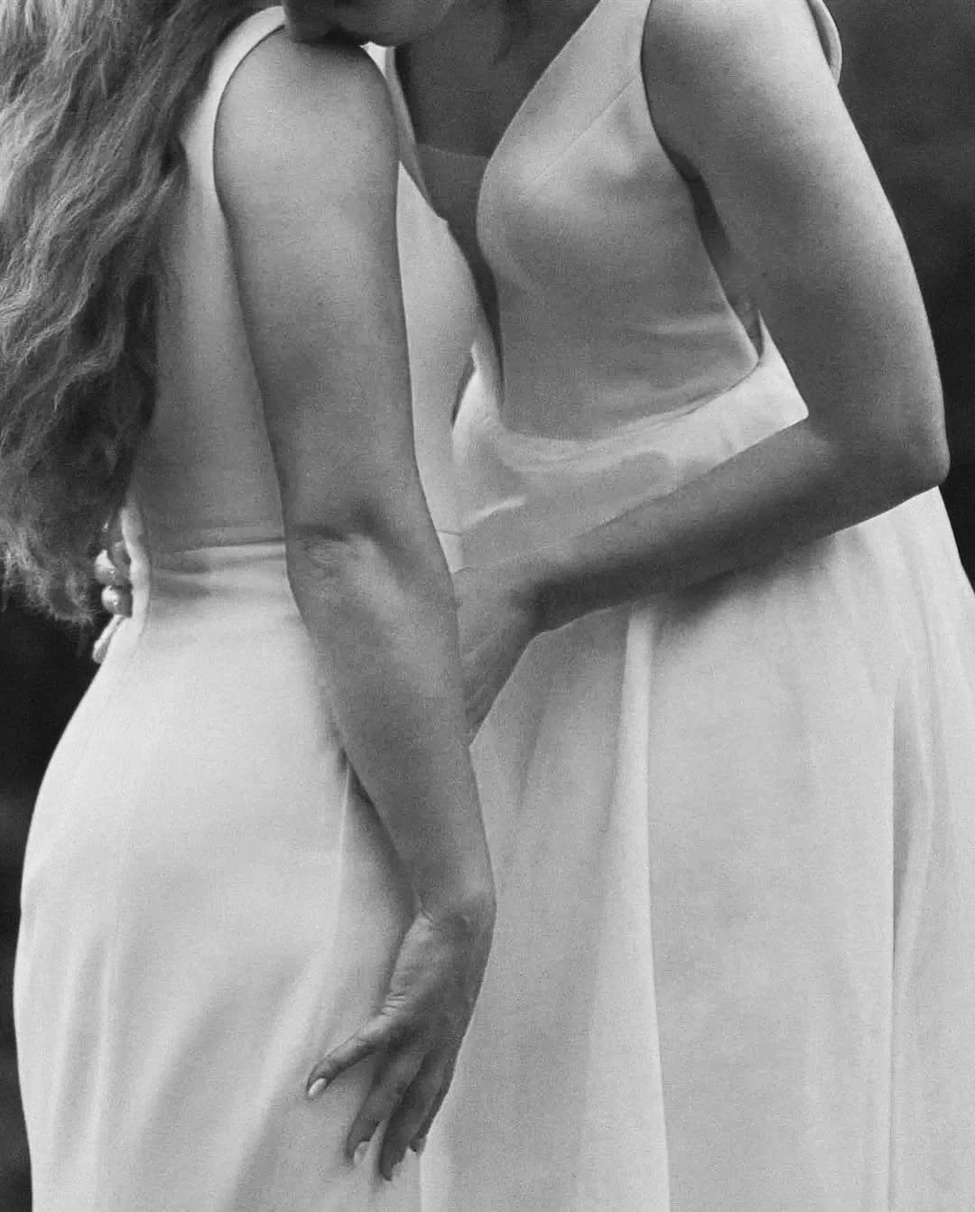 Close-up black and white photo of two women in sleeveless dresses, holding hands, standing close together.