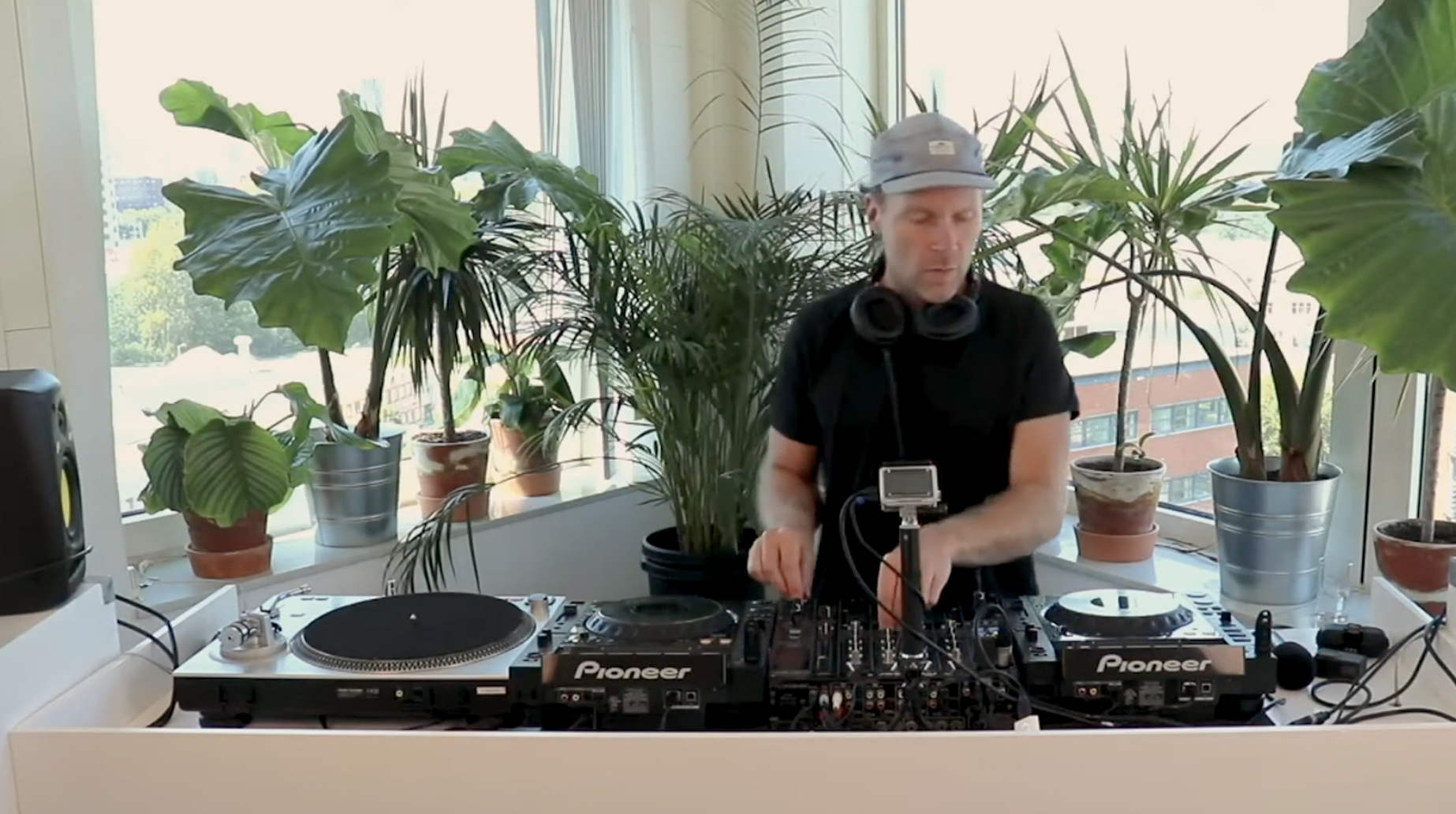 A man operating DJ equipment in a bright room with large windows and potted plants.
