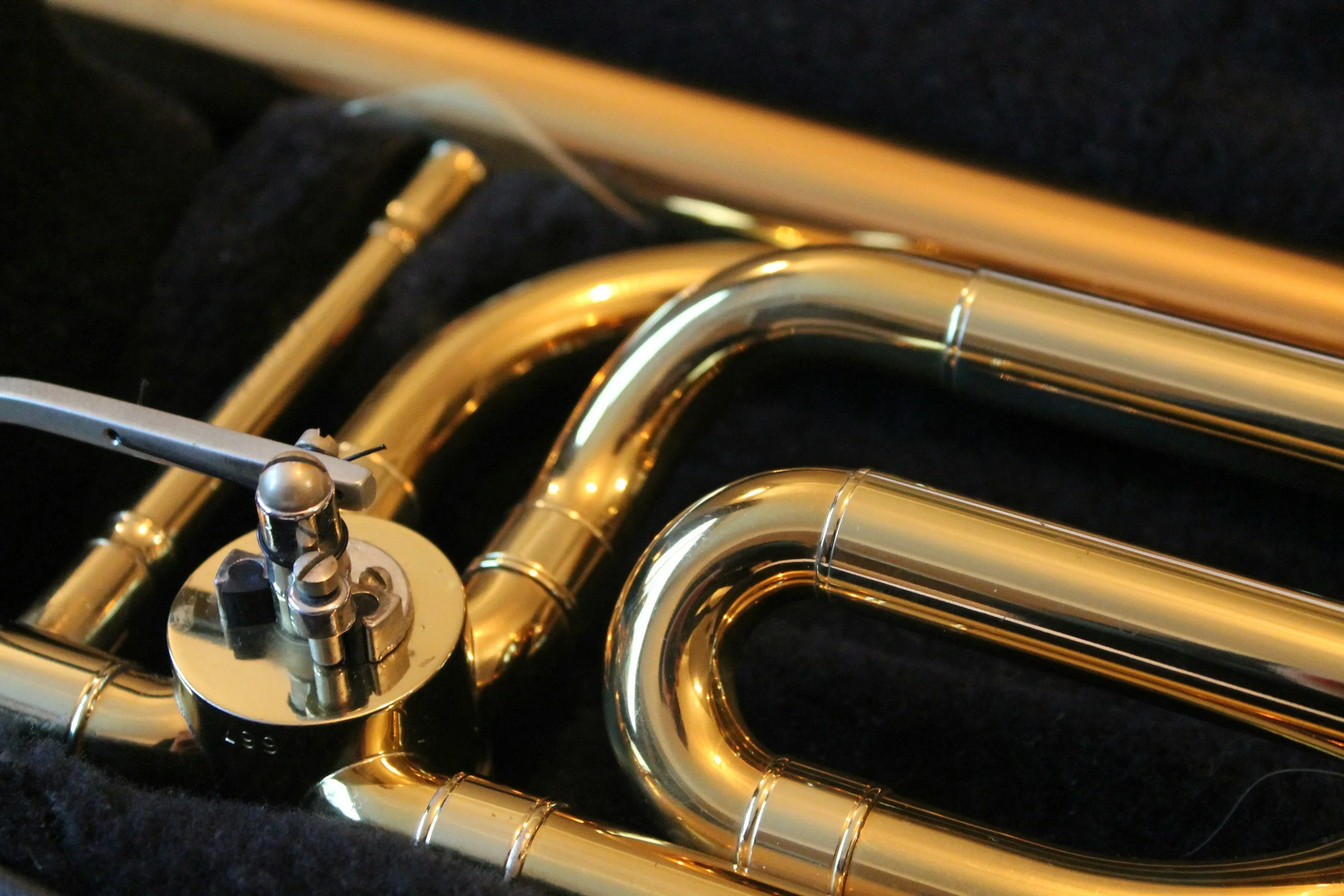 Close-up of a brass trumpet resting on a black surface, showing the valves and curved tubing with a shiny, reflective gold finish.