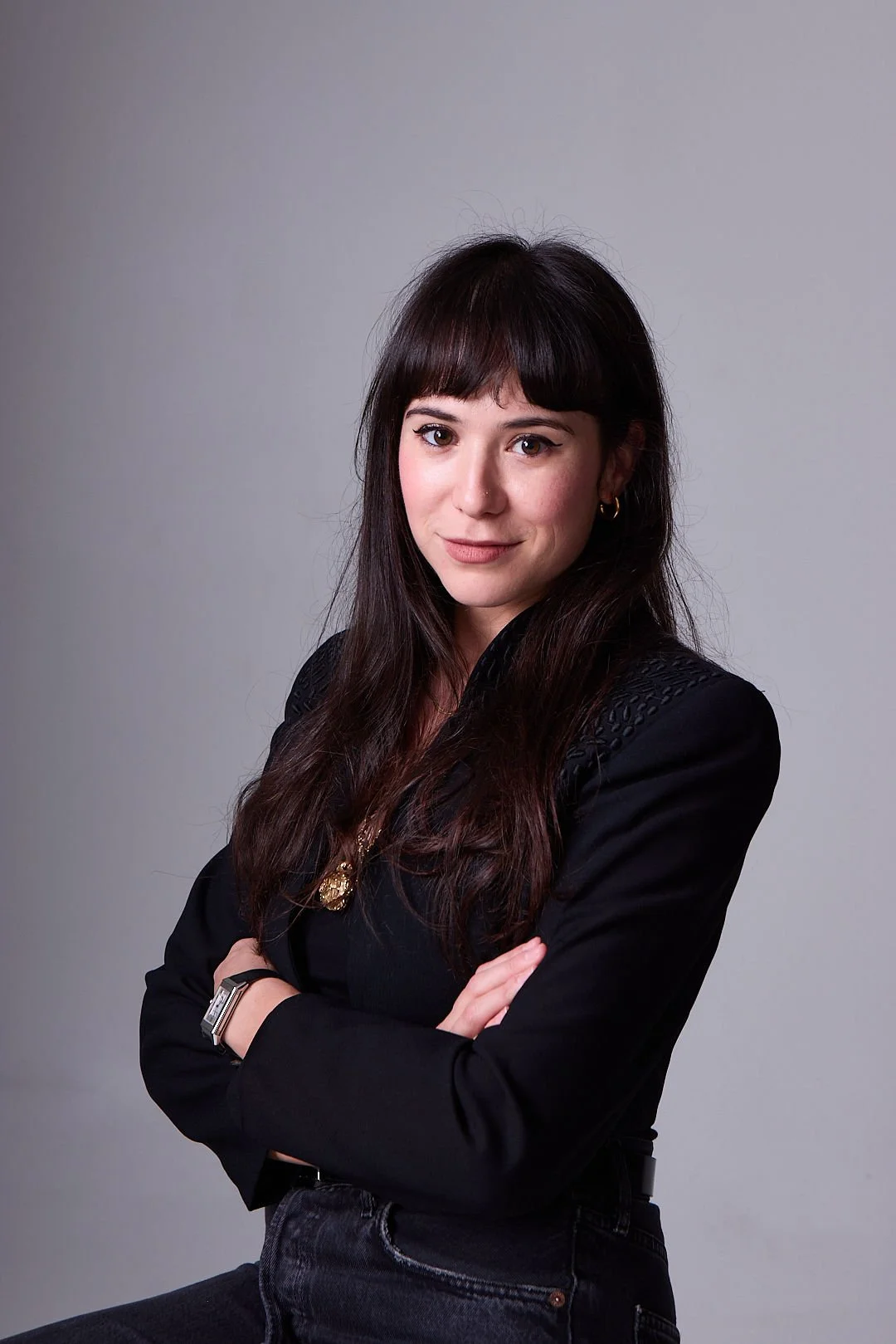 AJ Ayers, Writer, Speaker, and financial advisor, a woman with long dark hair, wearing a black blazer, with arms crossed, posing against a light gray background.