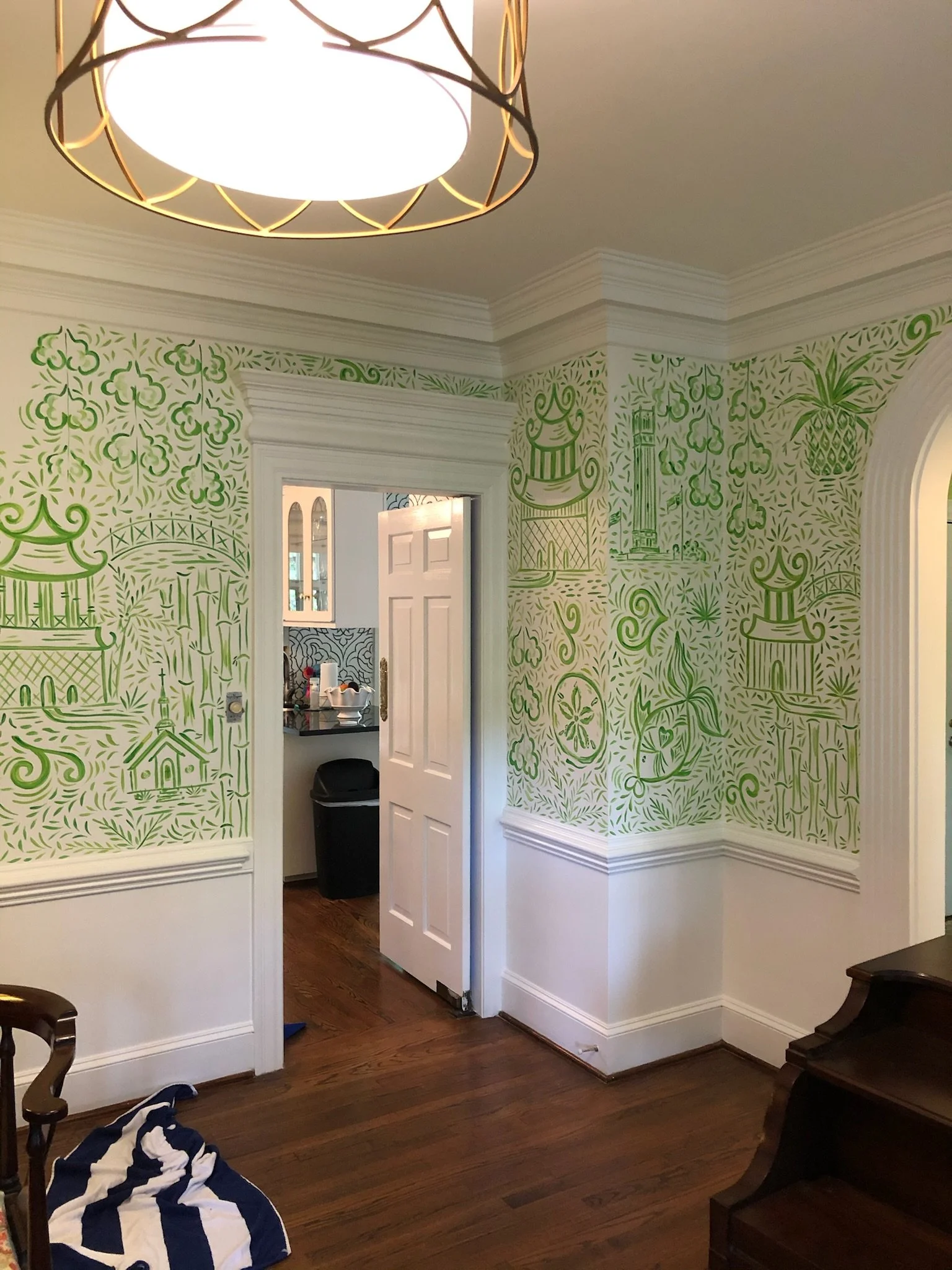 Room with green mural walls depicting various Asian-inspired pagodas, structures, and decorative elements, with a doorway leading to a kitchen area and a wooden floor.
