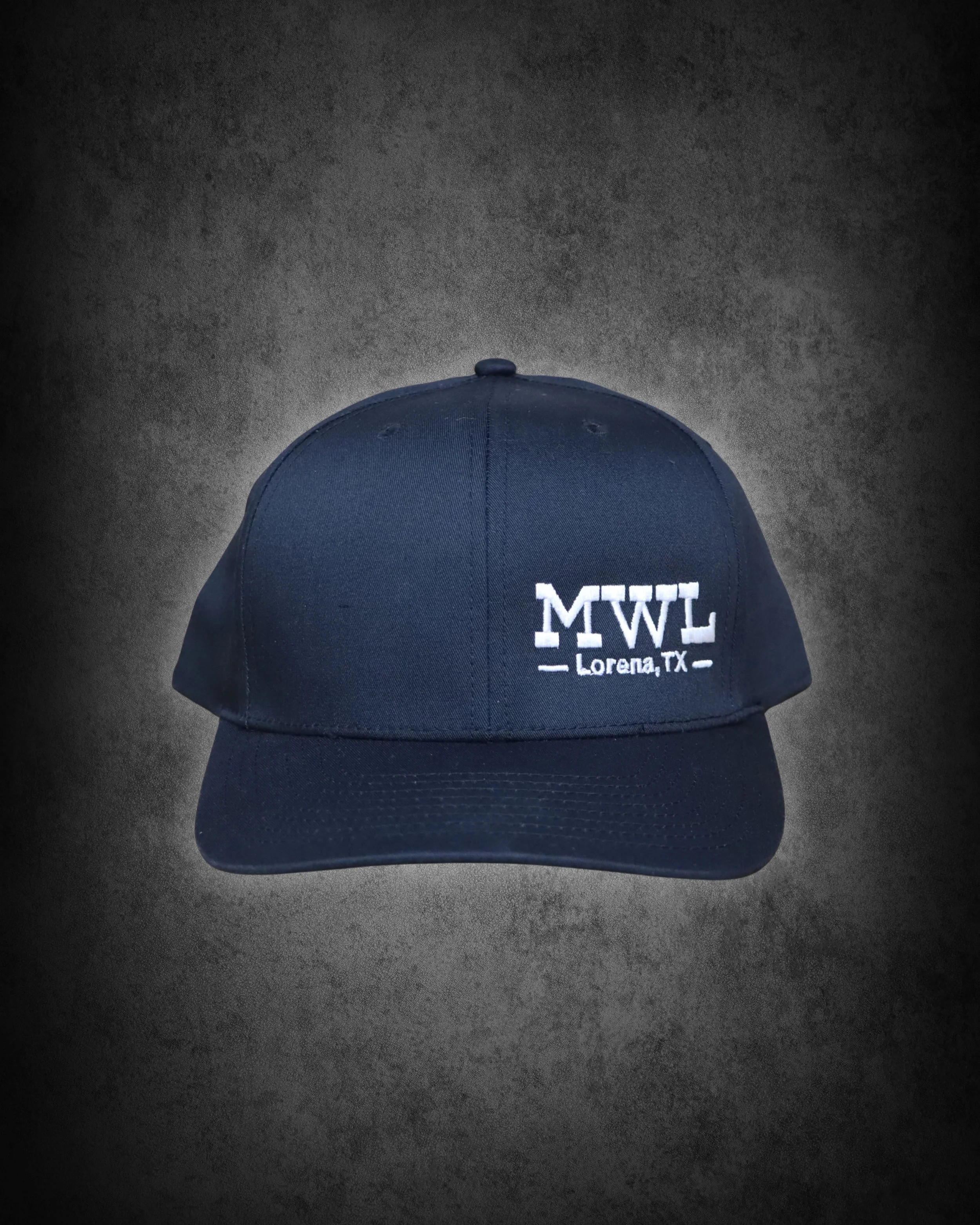 A navy blue baseball cap with white embroidered text that reads "LMLT" and "Lorena, TX" underneath, placed on a dark textured surface.