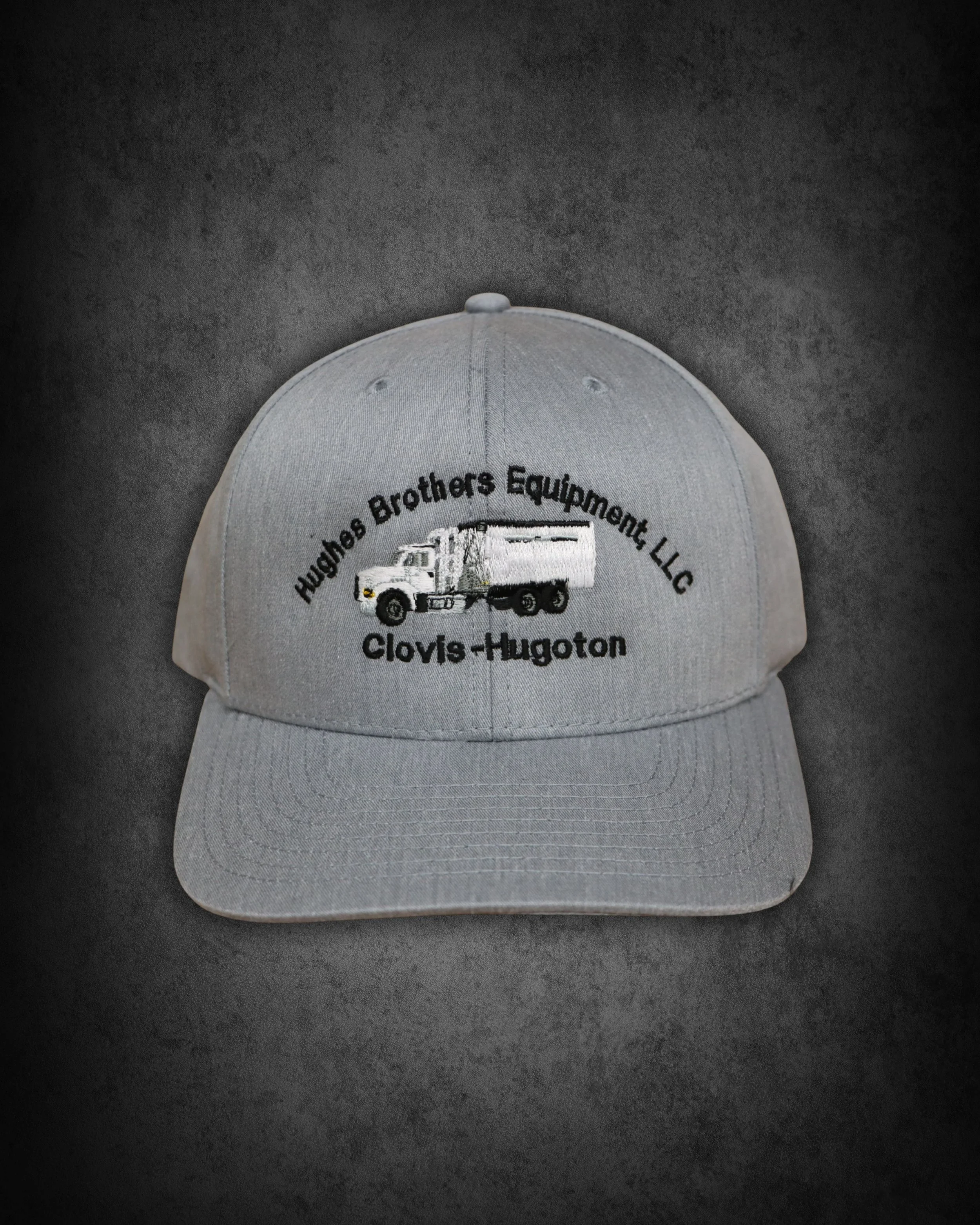 Gray baseball cap with embroidered logo and text on front, placed on dark surface.