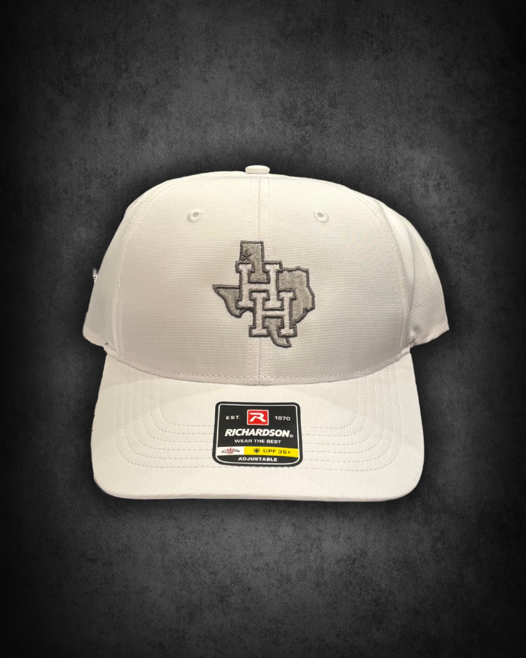 White Richardson adjustable baseball cap with a black and white embroidered interlocking H and L logo on the front. The cap has a sticker indicating it is UPF 35+, adjustable, and made by Richardson, established in 1970.