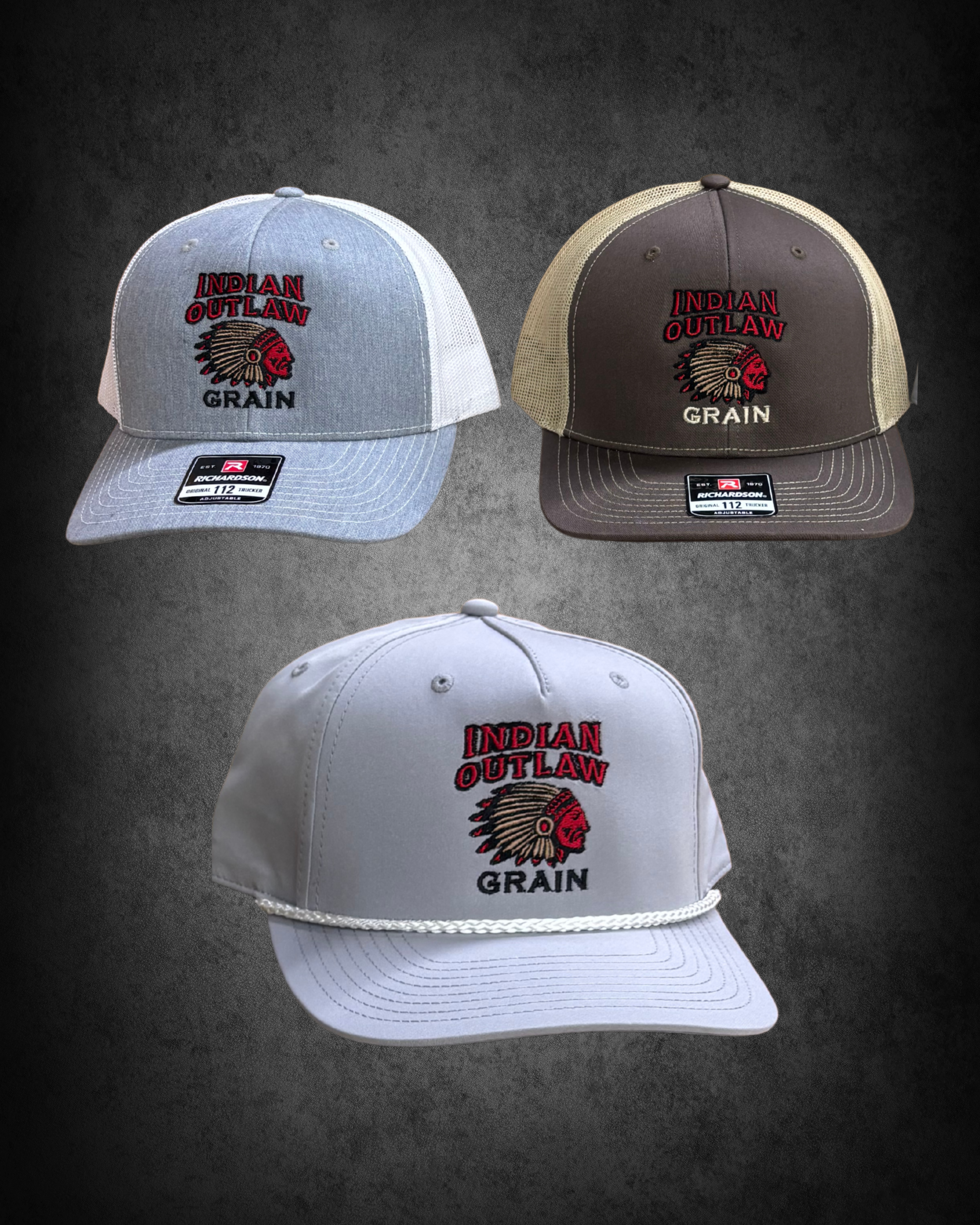 Two baseball caps with the 'Indian Outlaw Grain' logo, one gray and white, the other brown and beige, on a dark background.