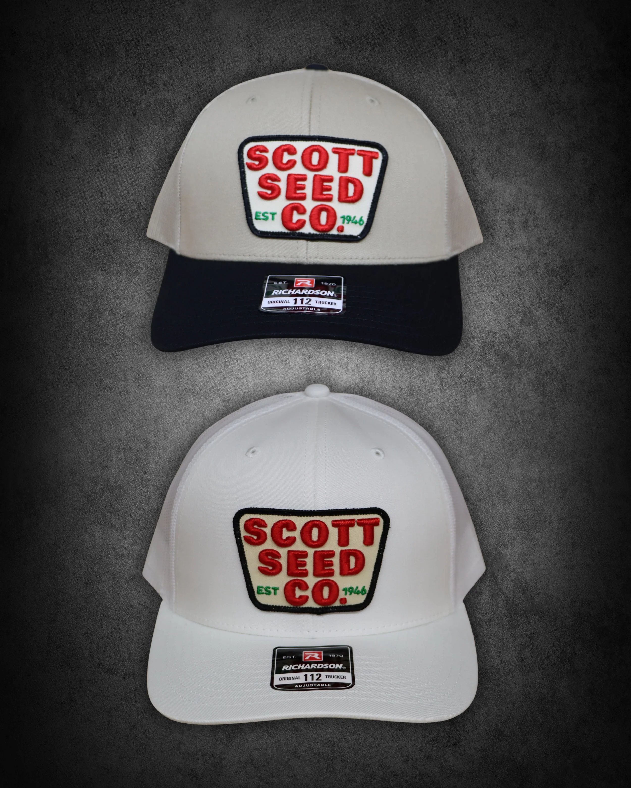Two baseball caps, one white and one black, with a patch reading 'Scott Seed Co.' and the establishment year 1946, placed on a gray surface.
