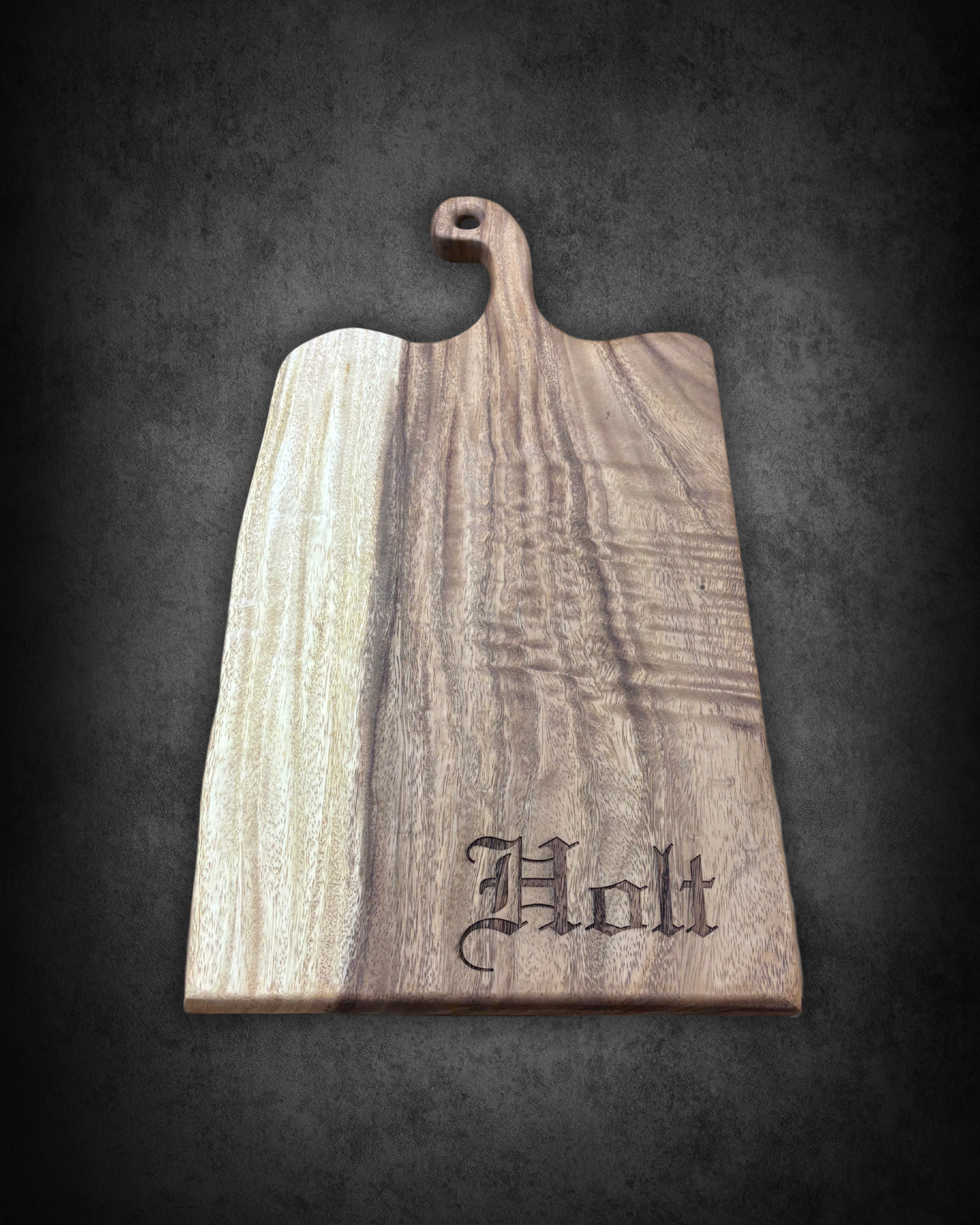 Wooden cutting board with engraved letters on a black surface.
