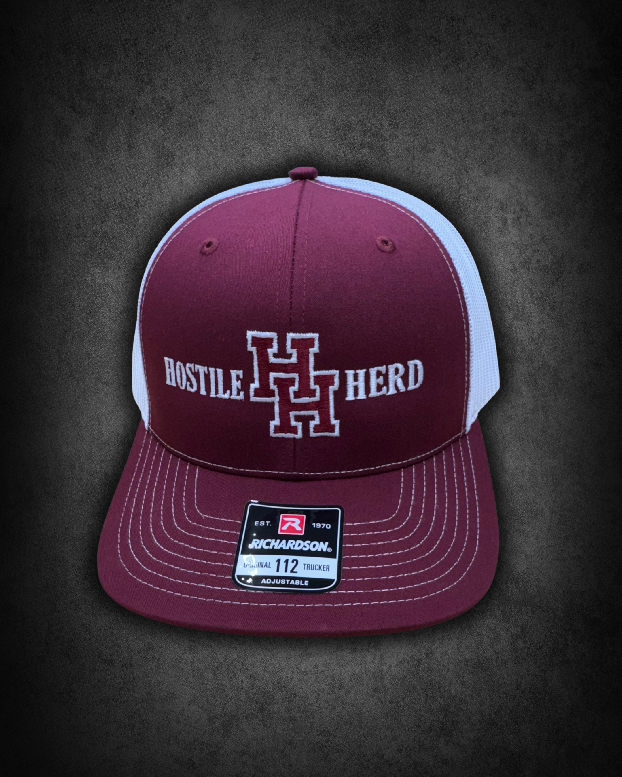 Maroon and white Richardson trucker cap with embroidered logo and text, placed on a black surface, displaying a size tag of 112.