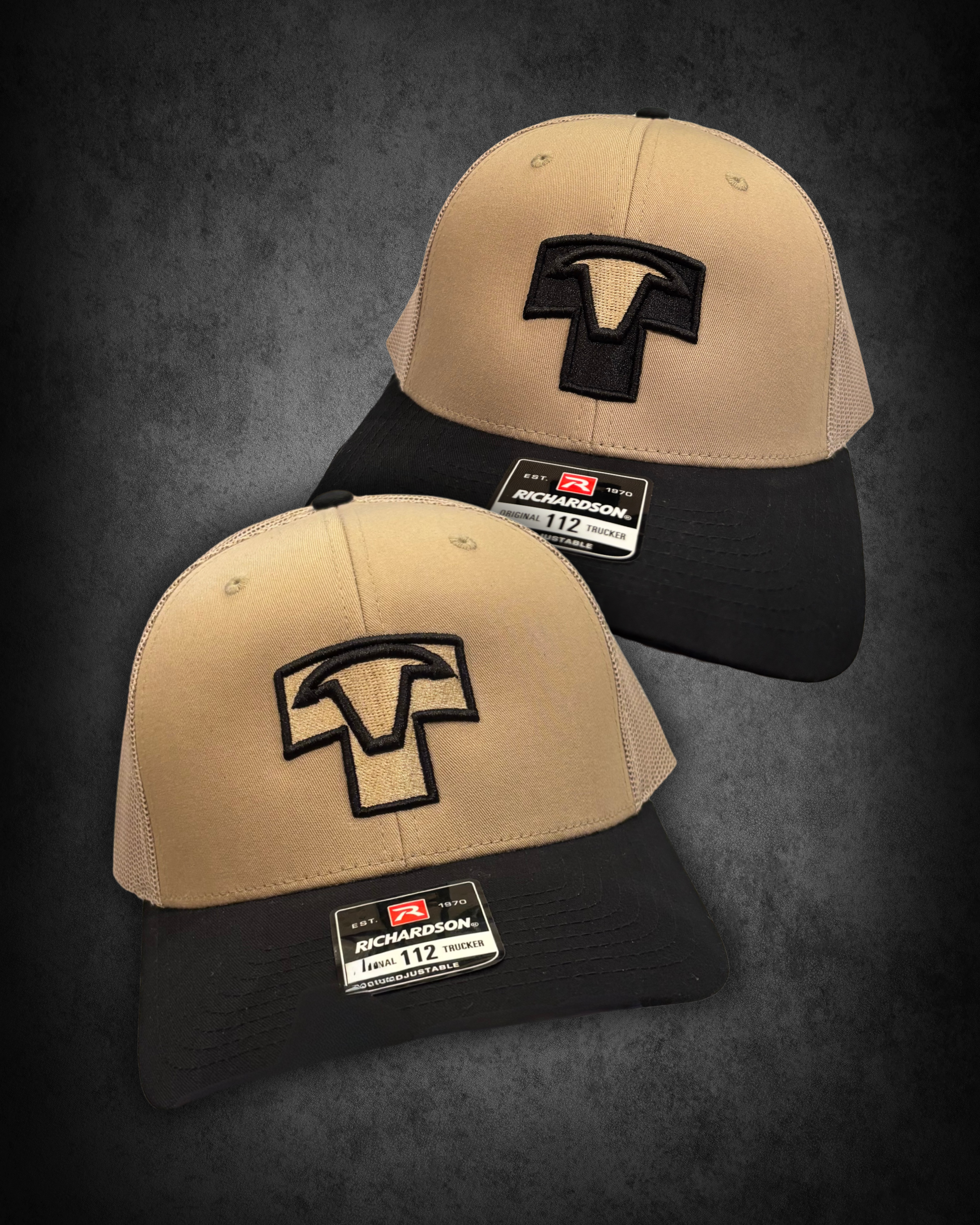 Two beige and black Richardson baseball caps with a black embroidered logo on the front, placed on top of black boxes with size tags reading "112" and brand labels, against a dark background.