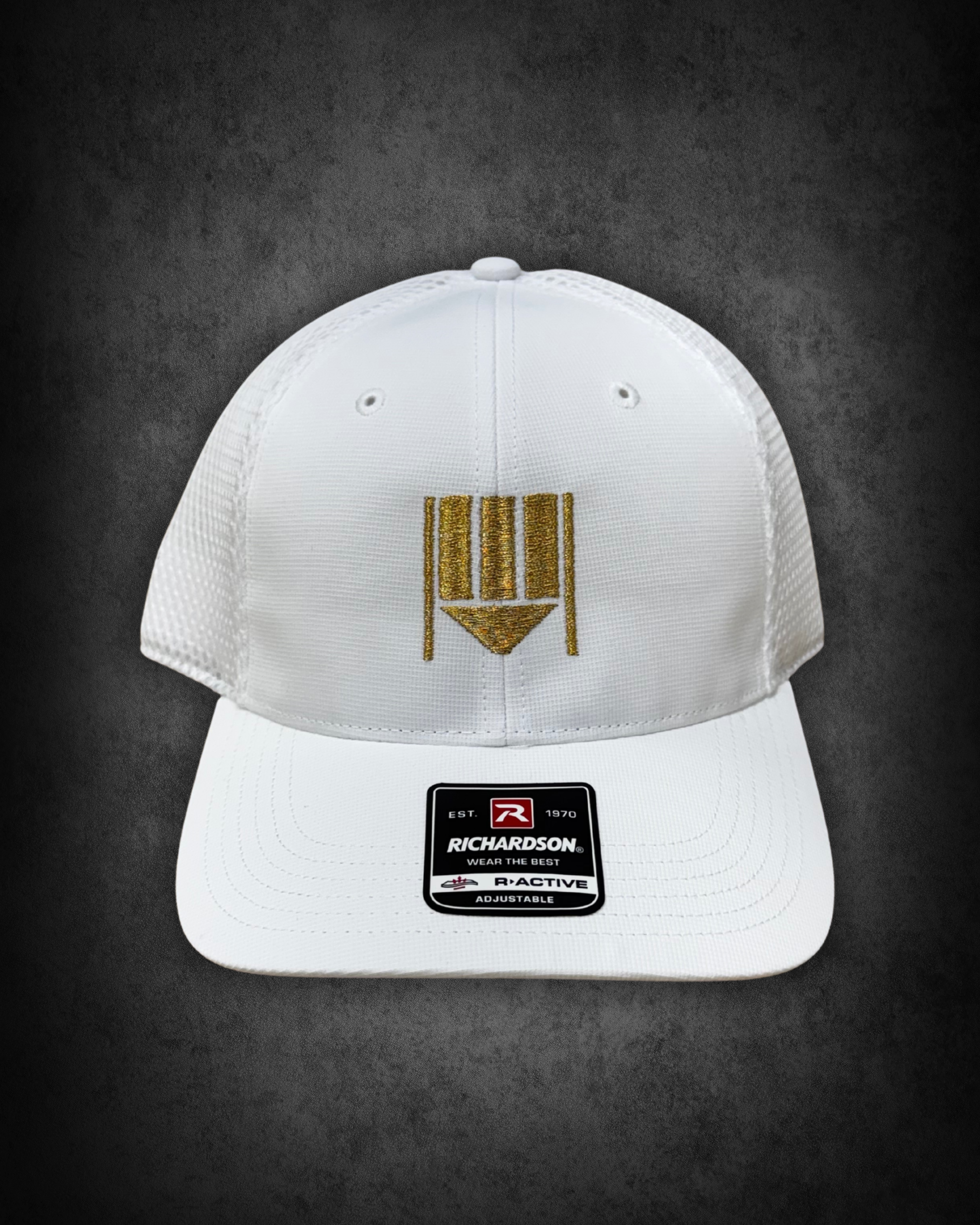 White Richardson baseball cap with gold embroidered logo and sticker on the brim, placed on a black background.