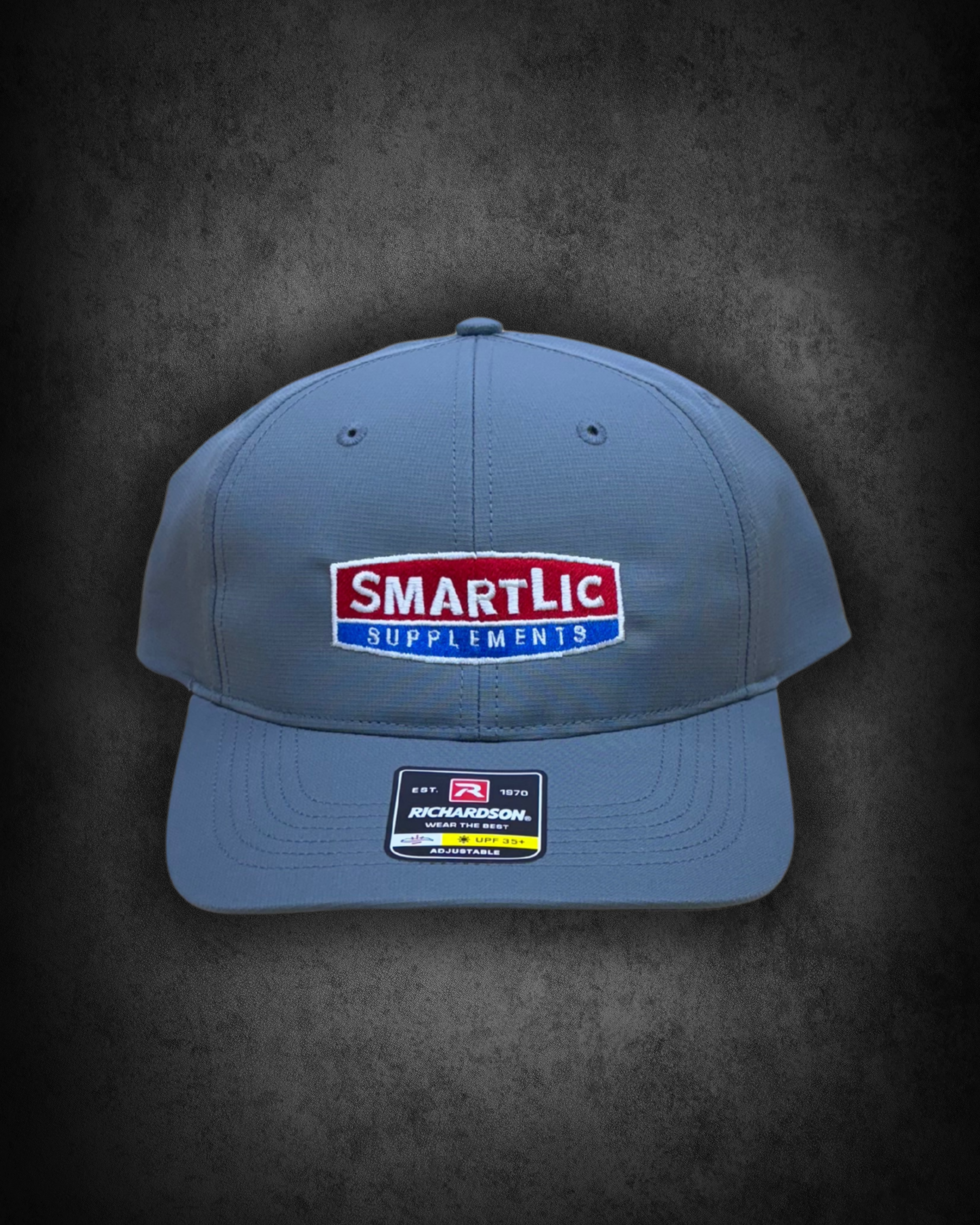 A gray baseball cap with a red, white, and blue logo that reads 'SMARTLIC SUPPLEMENTS' on the front, placed on a dark surface.