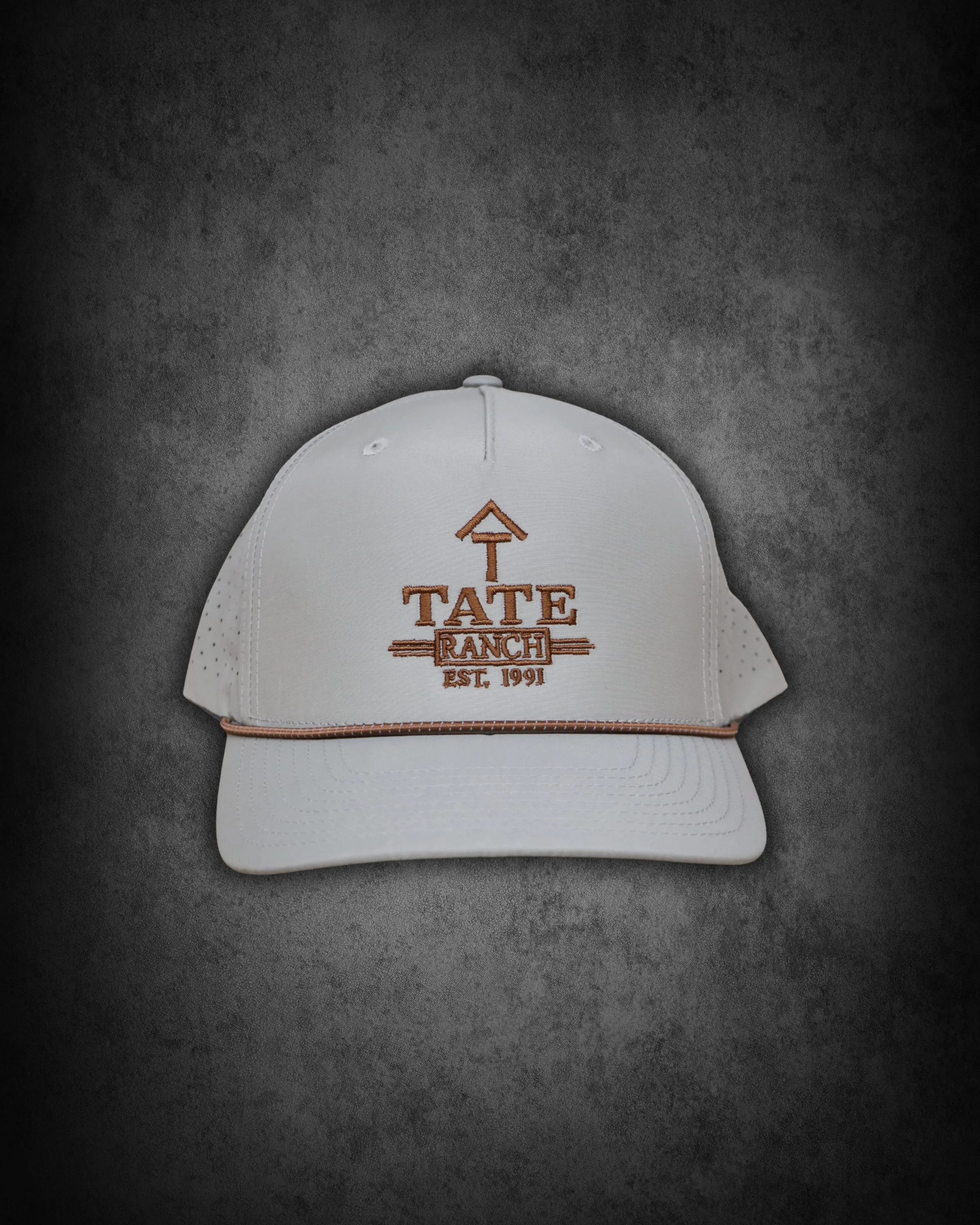 White baseball cap with orange embroidery reading "TATE RANCH EST. 1991" on a dark gray textured background.