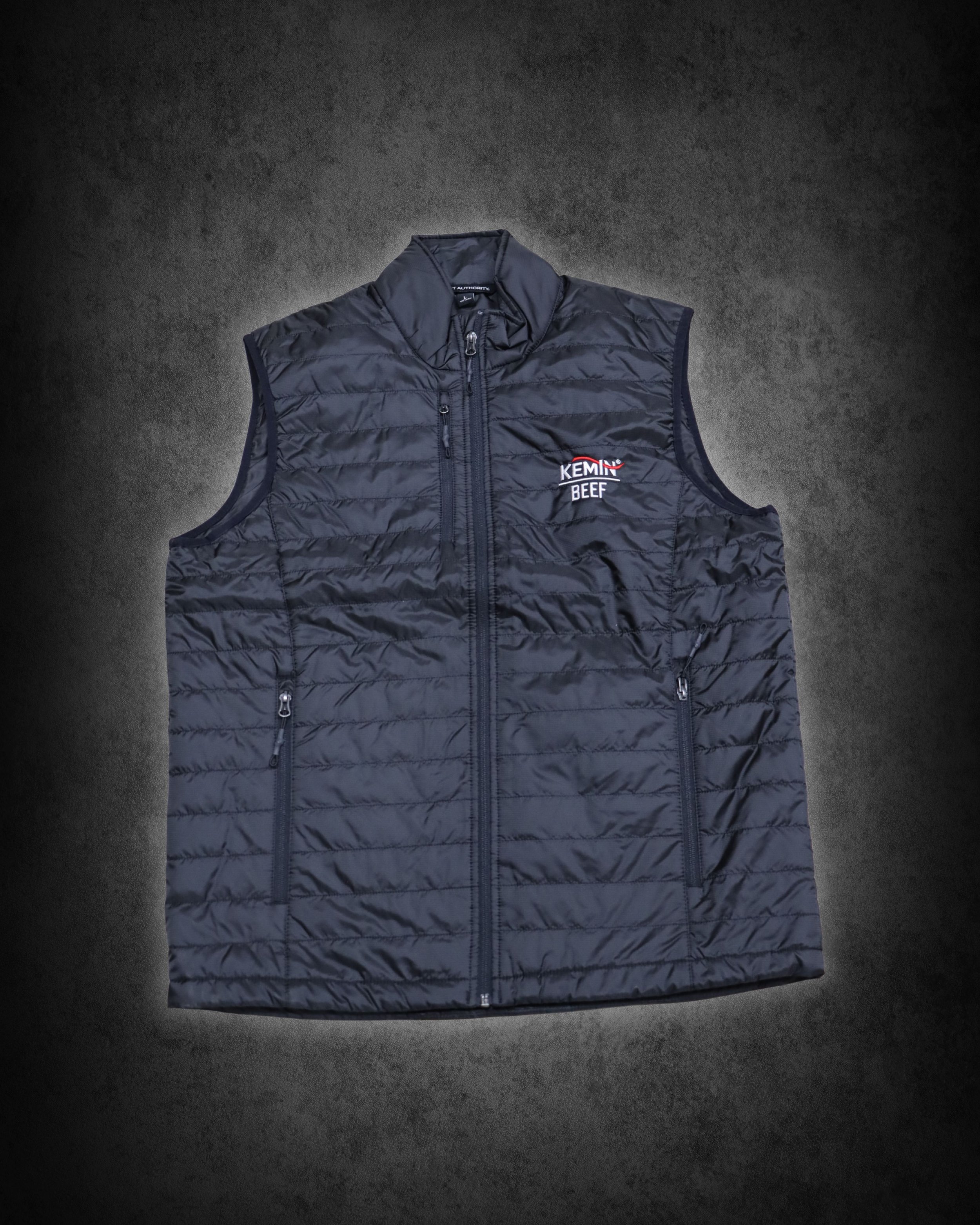 Black quilted vest with 'Kemlin Beef' logo on the left chest, lying flat on a dark surface with shadowed edges.