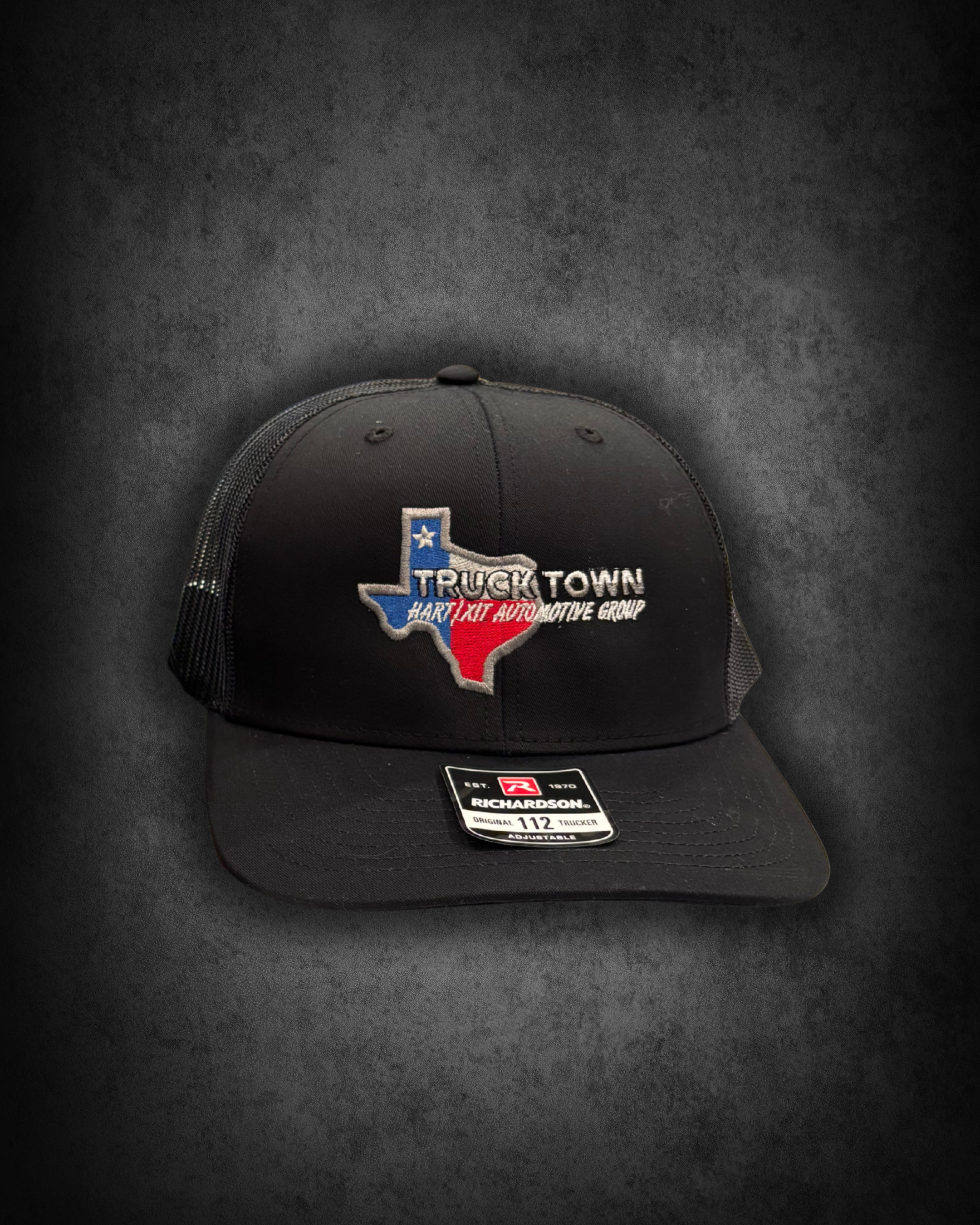 Black trucker cap with embroidered Texas outline and the words Truck Town, Hart TX Auto, and Group. Tag on brim indicating size 112, adjustable fit by Richardson.