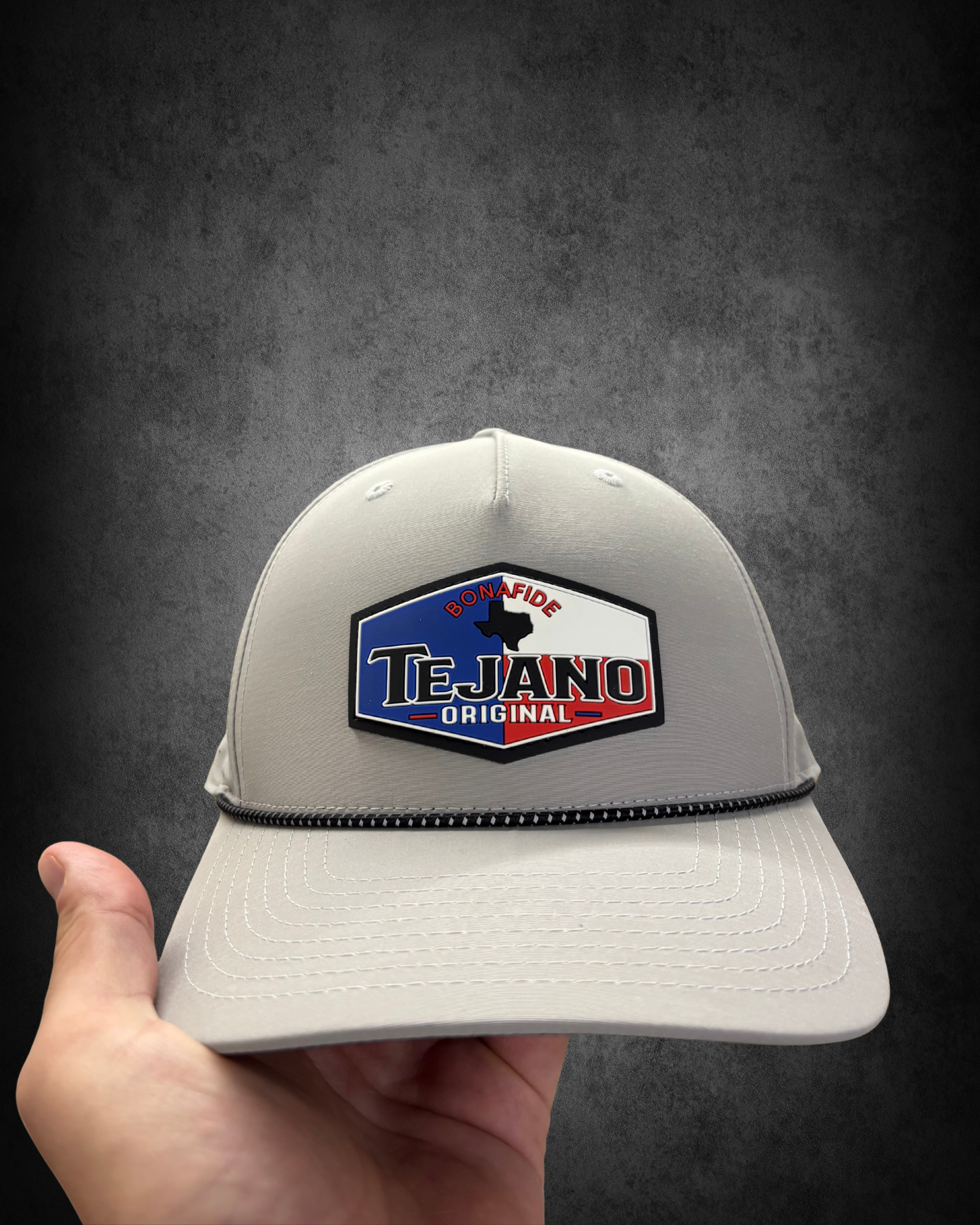A person holding a gray baseball cap with a black, red, and blue logo and Texas outline, on a black background.
