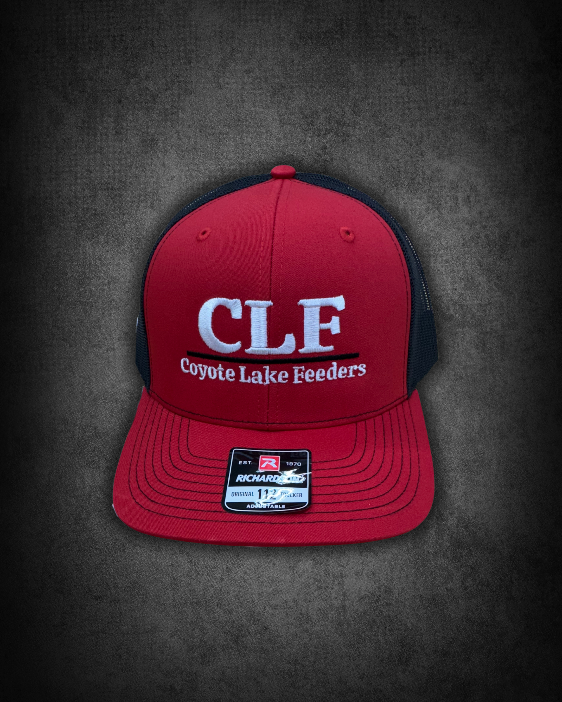 Red and black trucker cap with white embroidered text 'CFE' and 'Coyote Lake Feeders', on black surface, with a sticker on the brim indicating size 11 ½.