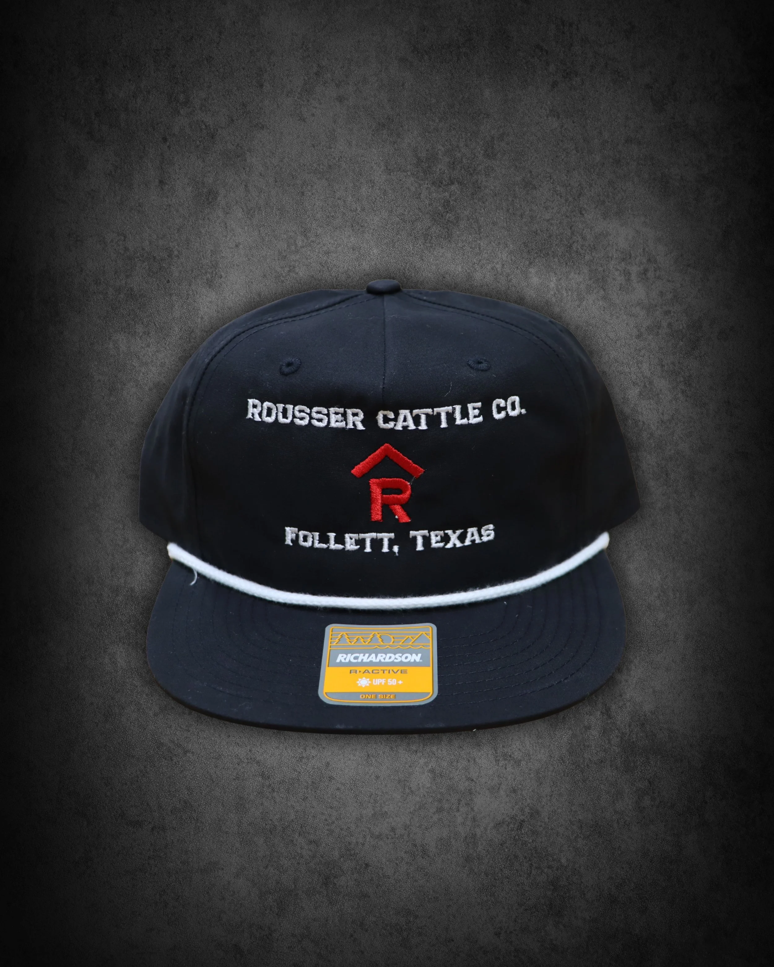 A black Richardson R-Active cap with a white and red embroidered logo and text, placed on a dark surface.