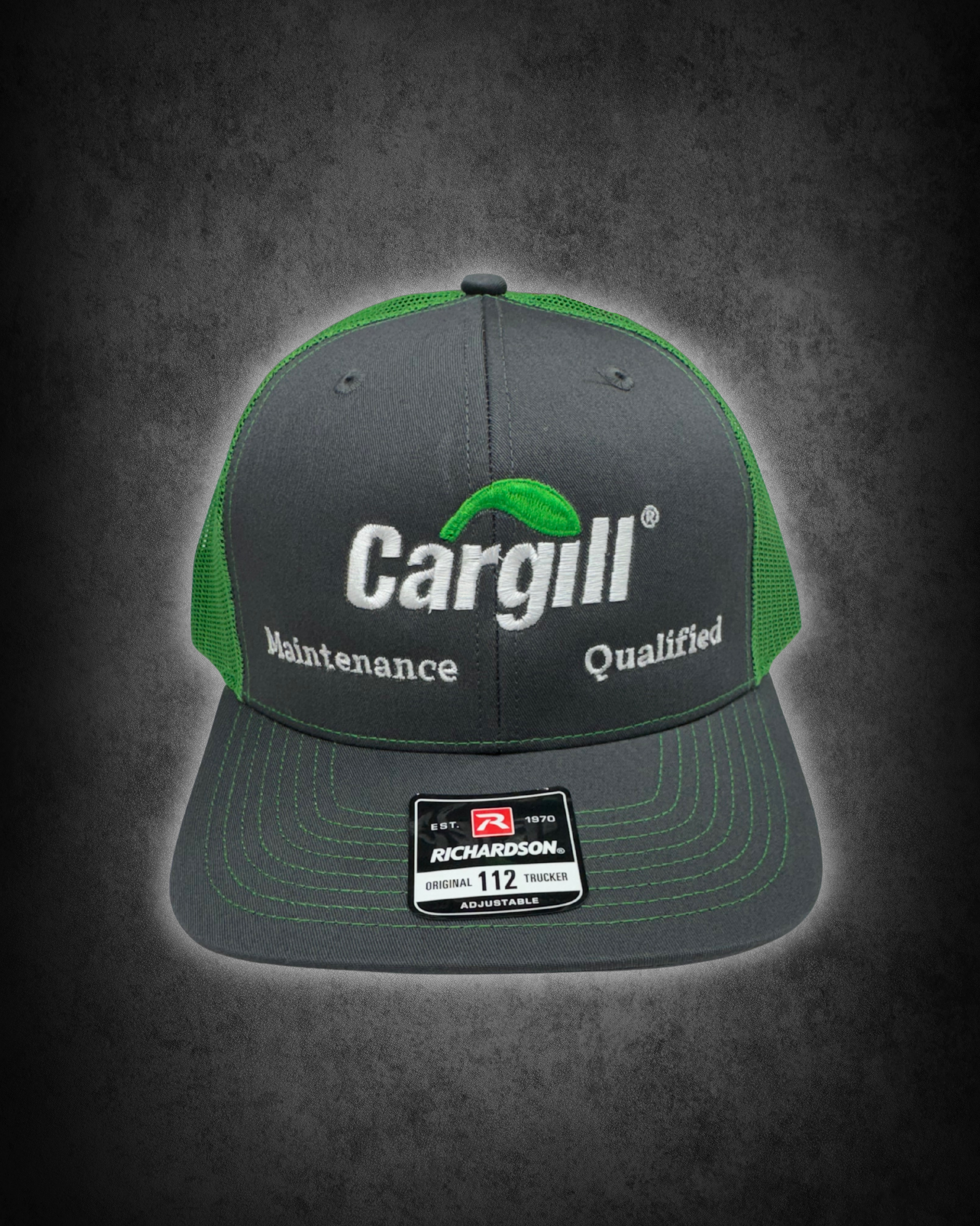 A black and green Richardson trucker hat with white embroidered text that reads "Cargill" and a green leaf logo. The cap features a mesh back and a sticker on the brim with the Richardson logo, model number 112, and size information.