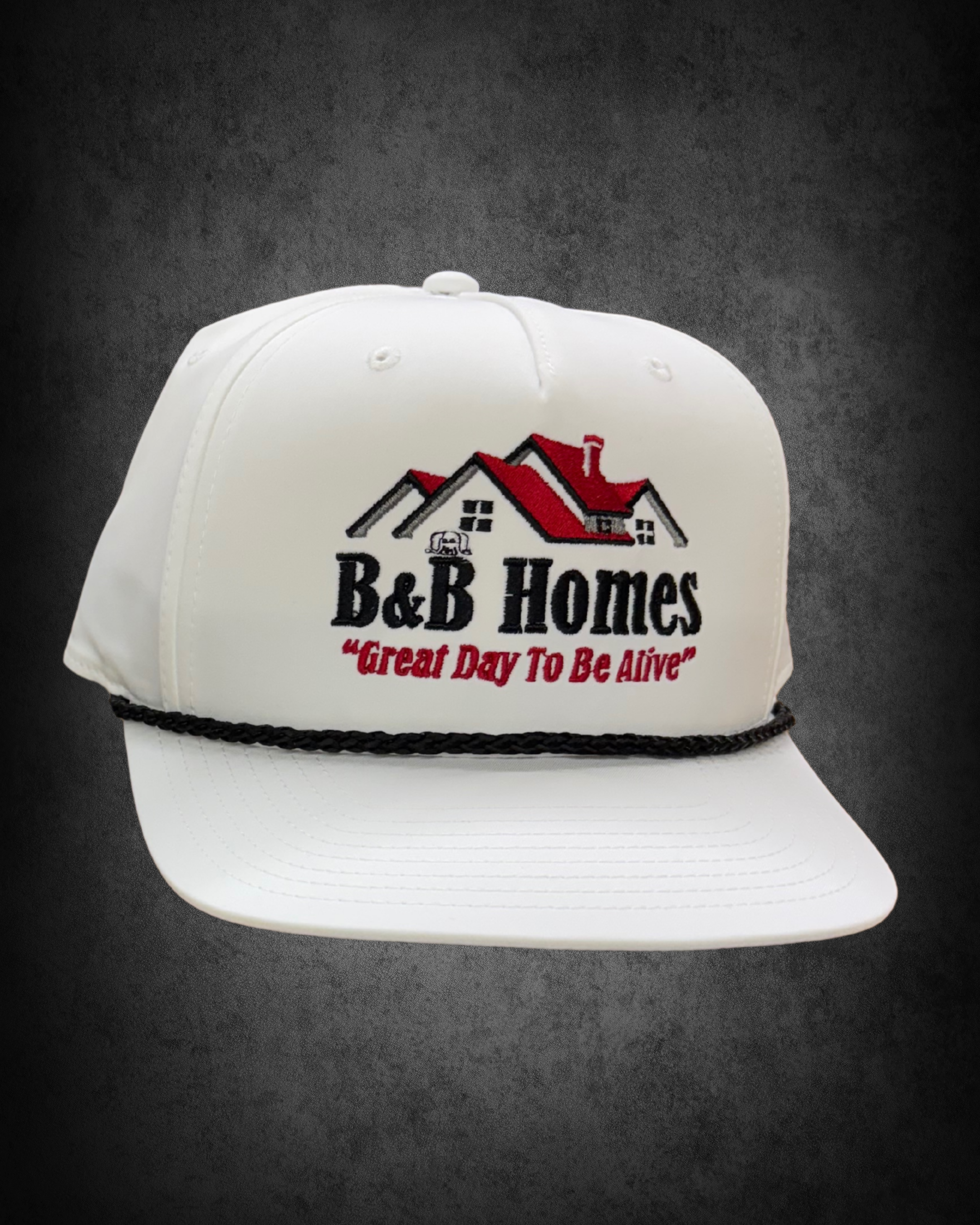 White baseball cap with embroidered logo of a house and trees, black text reading "BeB Homes," and red slogan "Great Day To Be Alive," placed on a black textured surface.