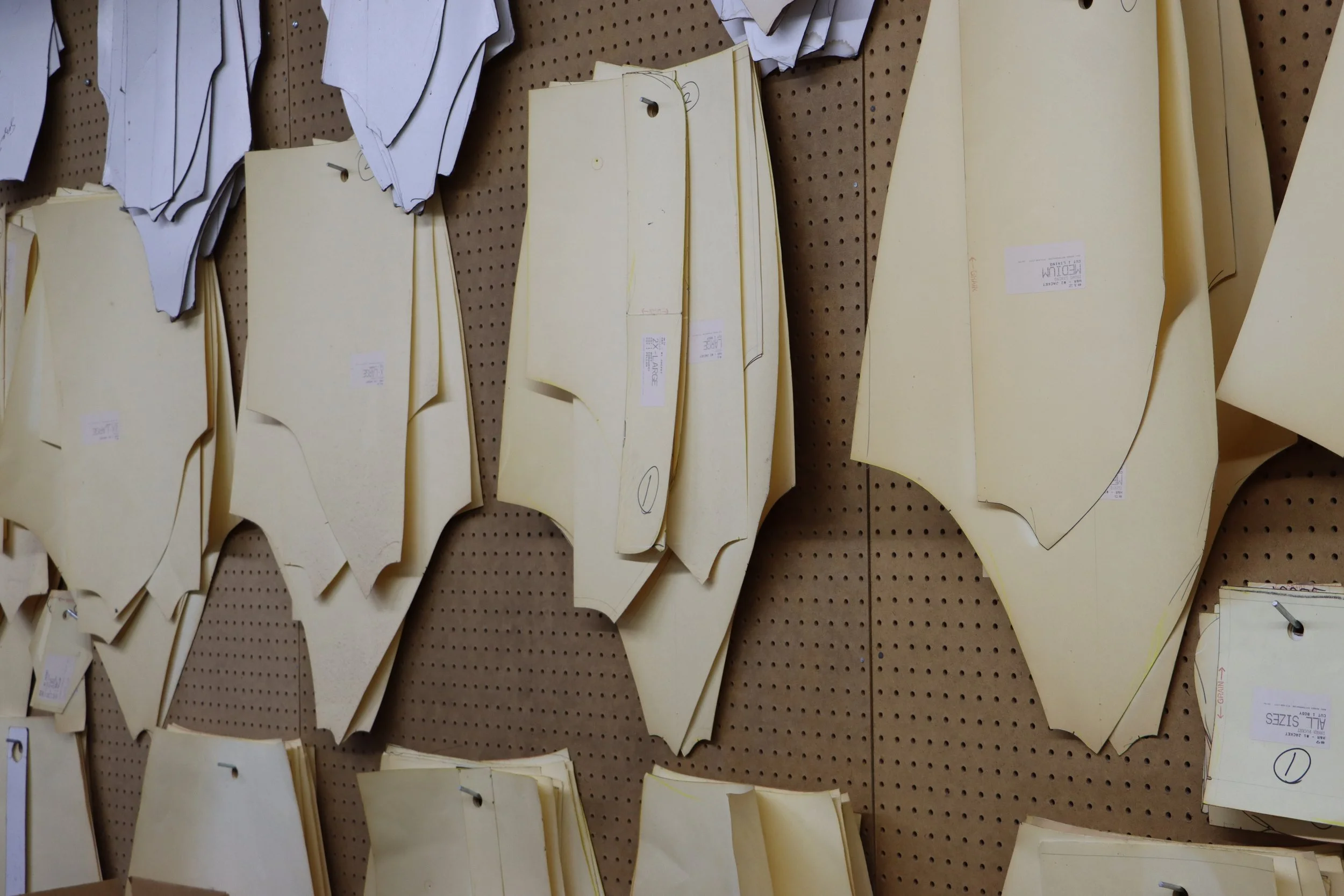 Patterns of fabric or paper with yellow colored sheets and some black markings, pinned or clipped to a pegboard background.