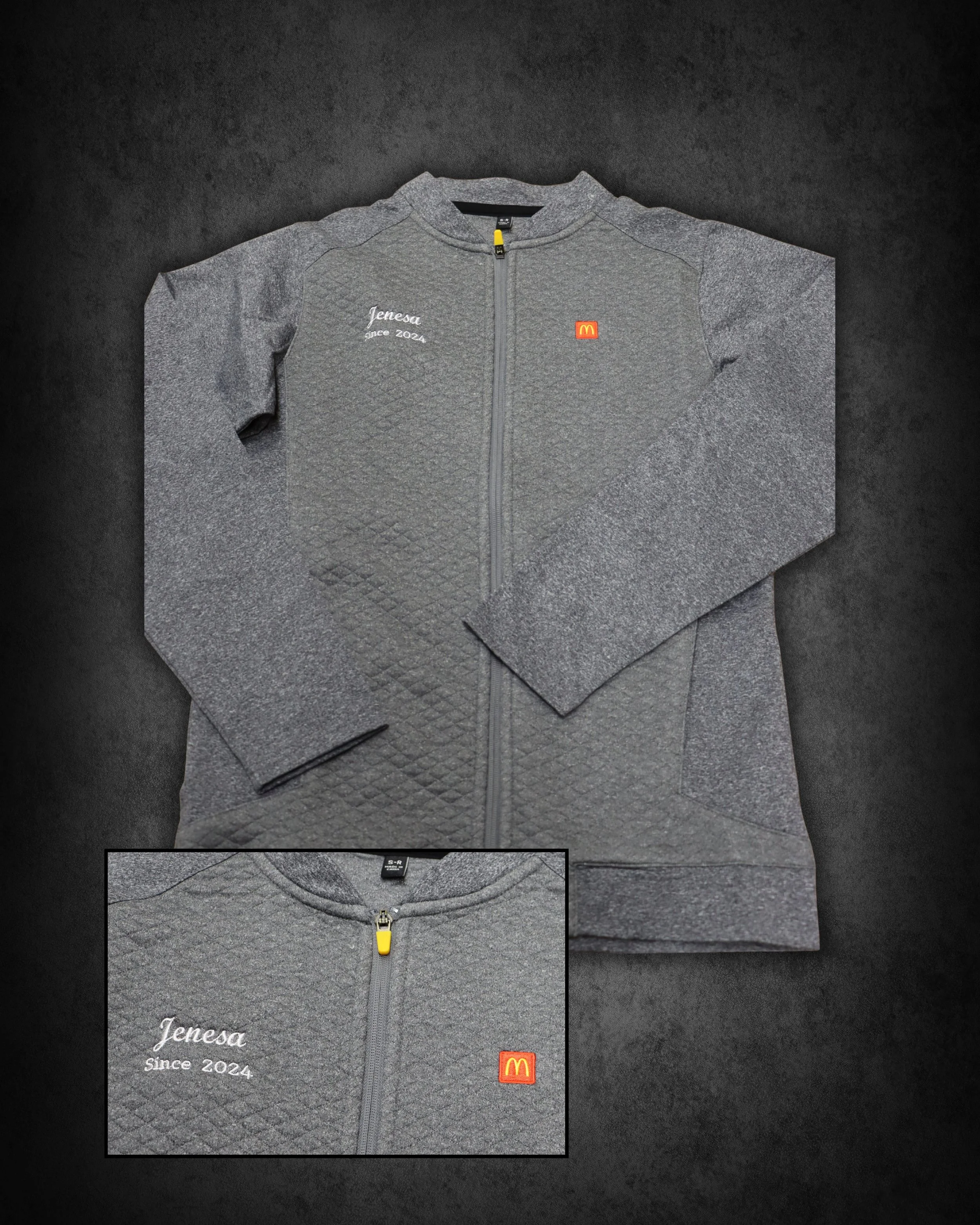 Gray zip-up jacket with embroidered name 'Jenesa' and 'since 2024' on the left chest, and a small McDonald's logo on the right chest, lying on a dark surface.