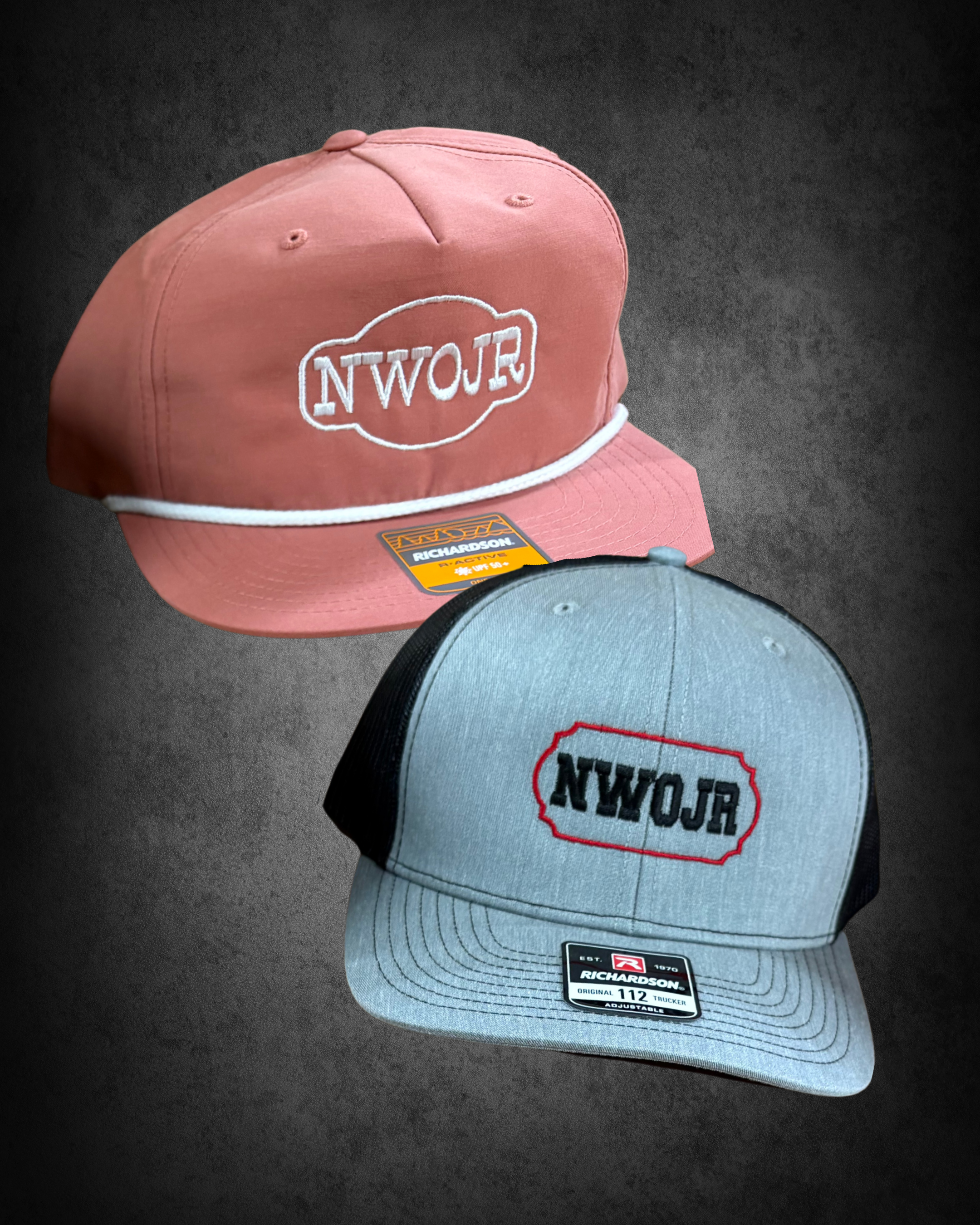 A pink baseball cap with white embroidery that reads "NWOR" and a yellow sticker on the brim. A gray baseball cap with black mesh back and red and black tag reading "Richardson" and "112" is in front of it. Both caps are on a dark surface.