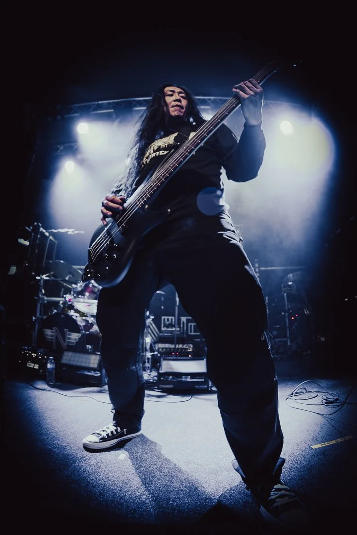 Low-angle cinematic shot of a bassist on stage with atmospheric blue backlighting. High-contrast concert photography and visual branding for artists.