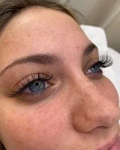 Close-up of a woman's face showing her blue eyes, eyebrows, and part of her nose and cheek.