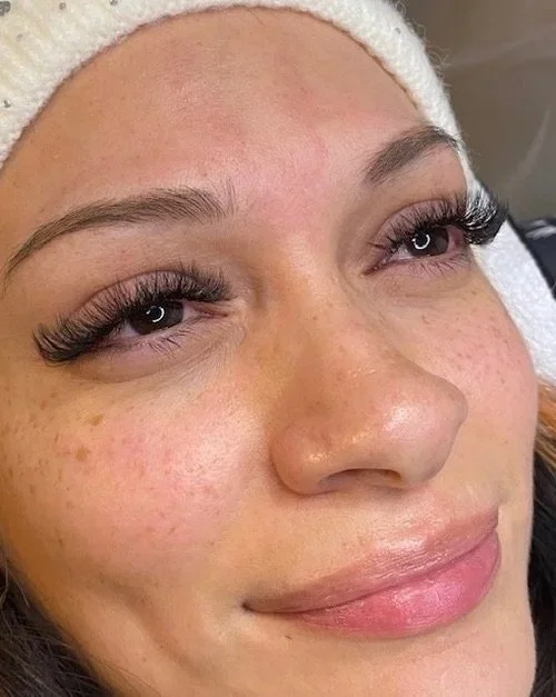 Close-up of a woman's face with eyelash extensions, light makeup, and a white towel headband.