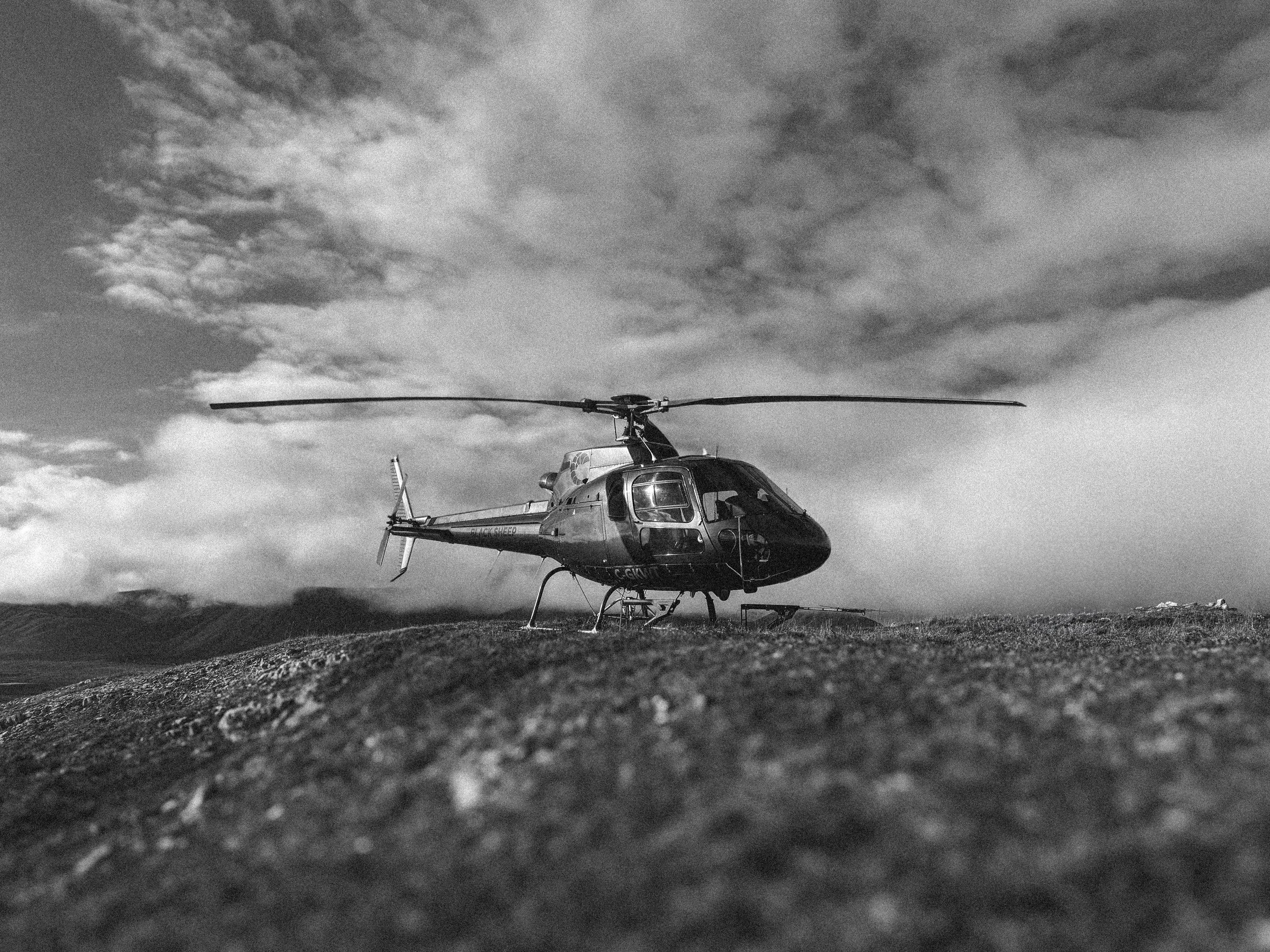 Black and white photo of a helicopter on a rocky terrain with cloudy sky in the background.
