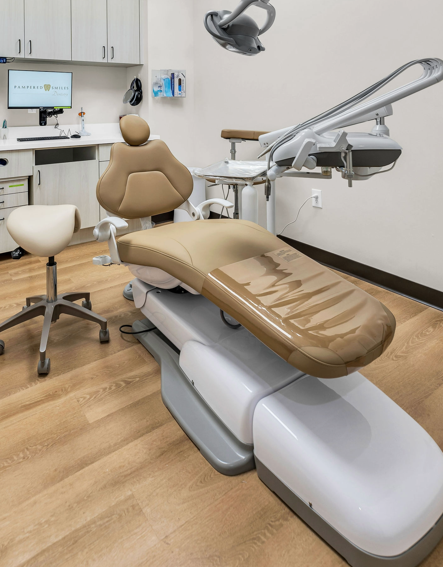 Dental examination room with an adjustable dental chair, overhead light, stool, and dental equipment.