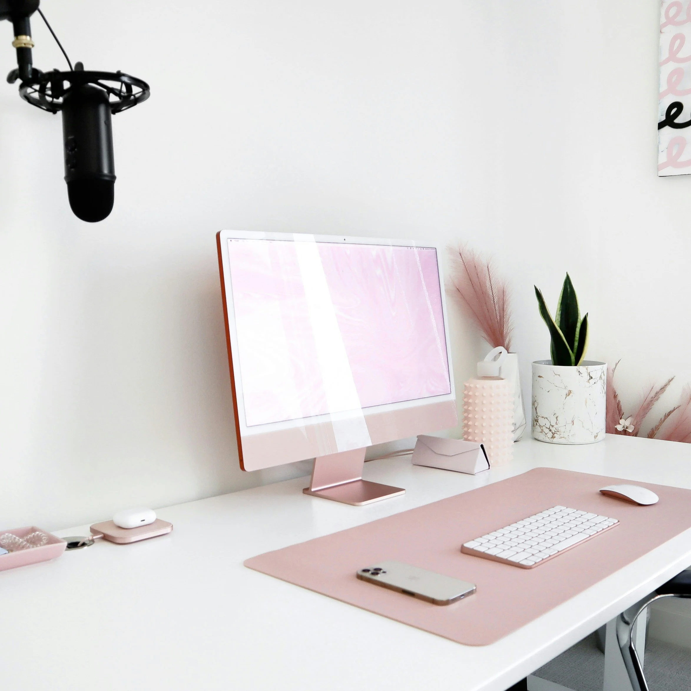 Desk setup with pink and white tech accessories, potted plants, and decor on a white desk in a minimalist workspace.