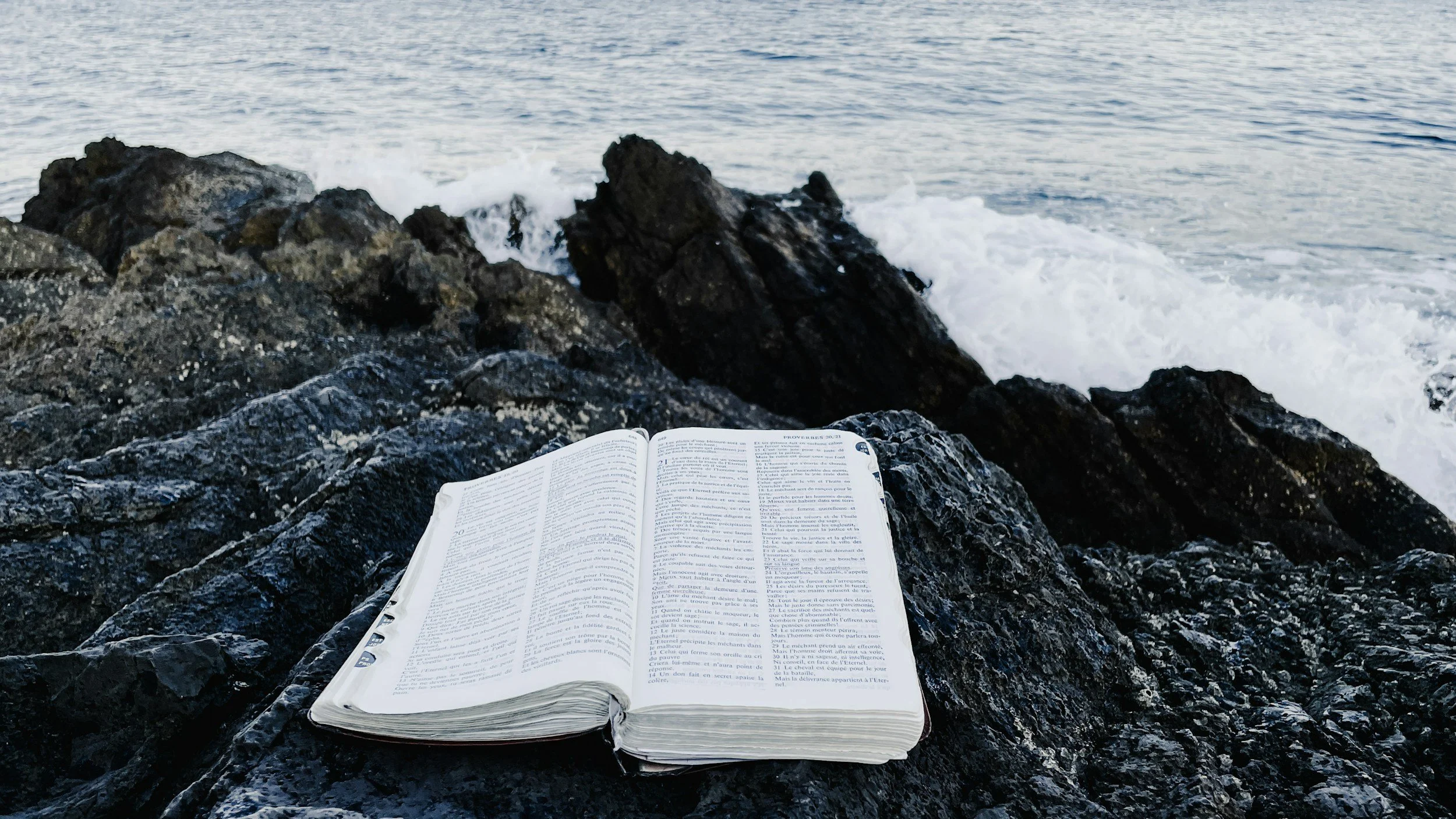 bible on rocks in front of ocean